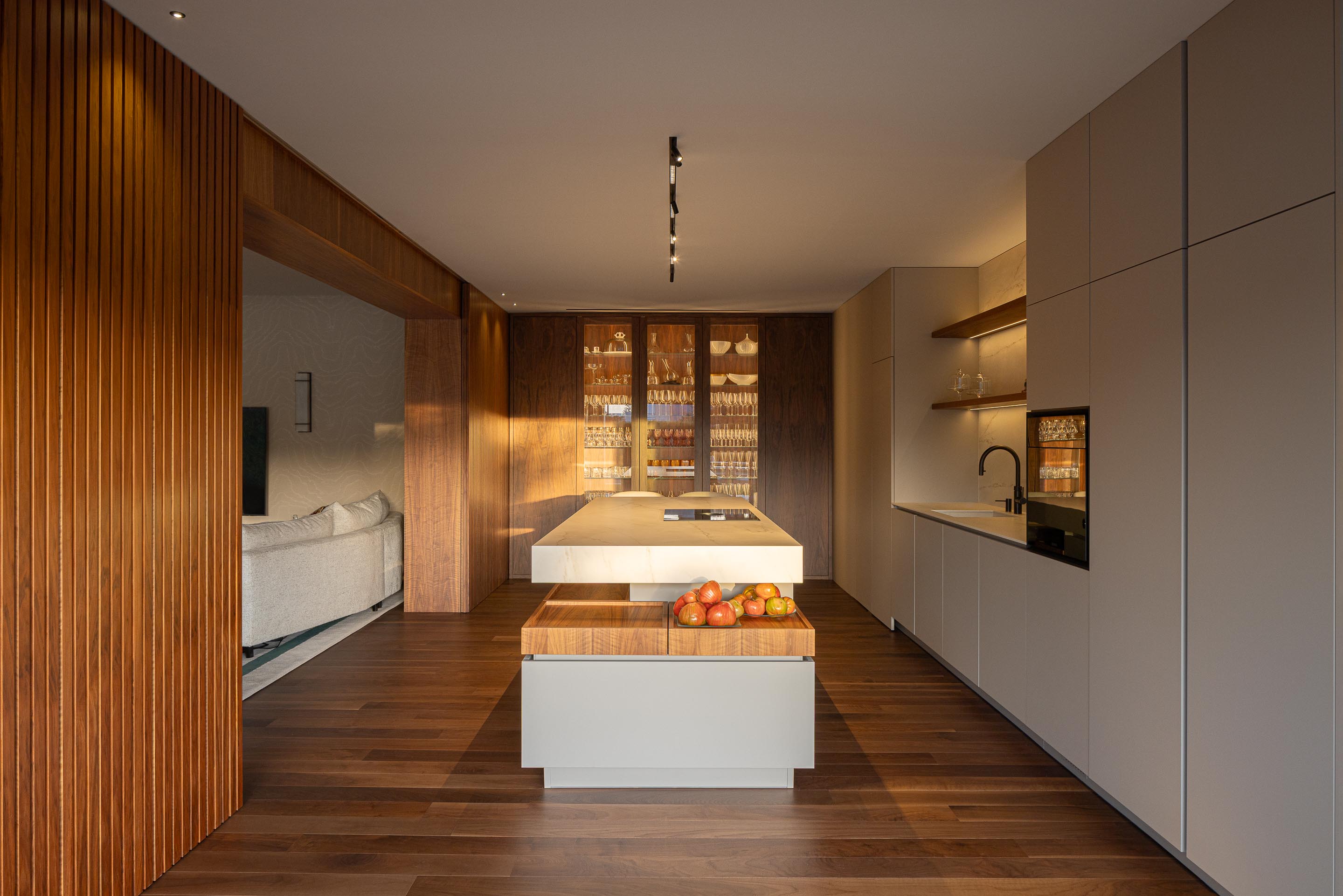 Cozinha: Ilha central com bancada em mármore branco, armários brancos e parede revestida em ripas de madeira escura. — Casa do Engenho arquitetura silverline em Vila Nova de Gaia