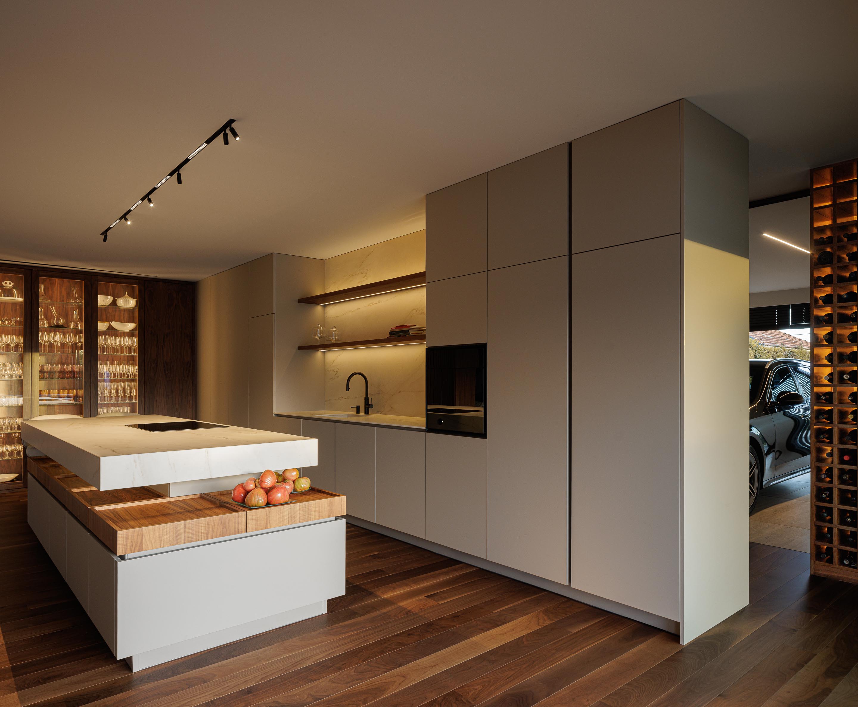Cozinha: Ilha central com bancada em mármore branco, armários brancos e garrafeira ao fundo. — Casa do Engenho arquitetura silverline em Vila Nova de Gaia