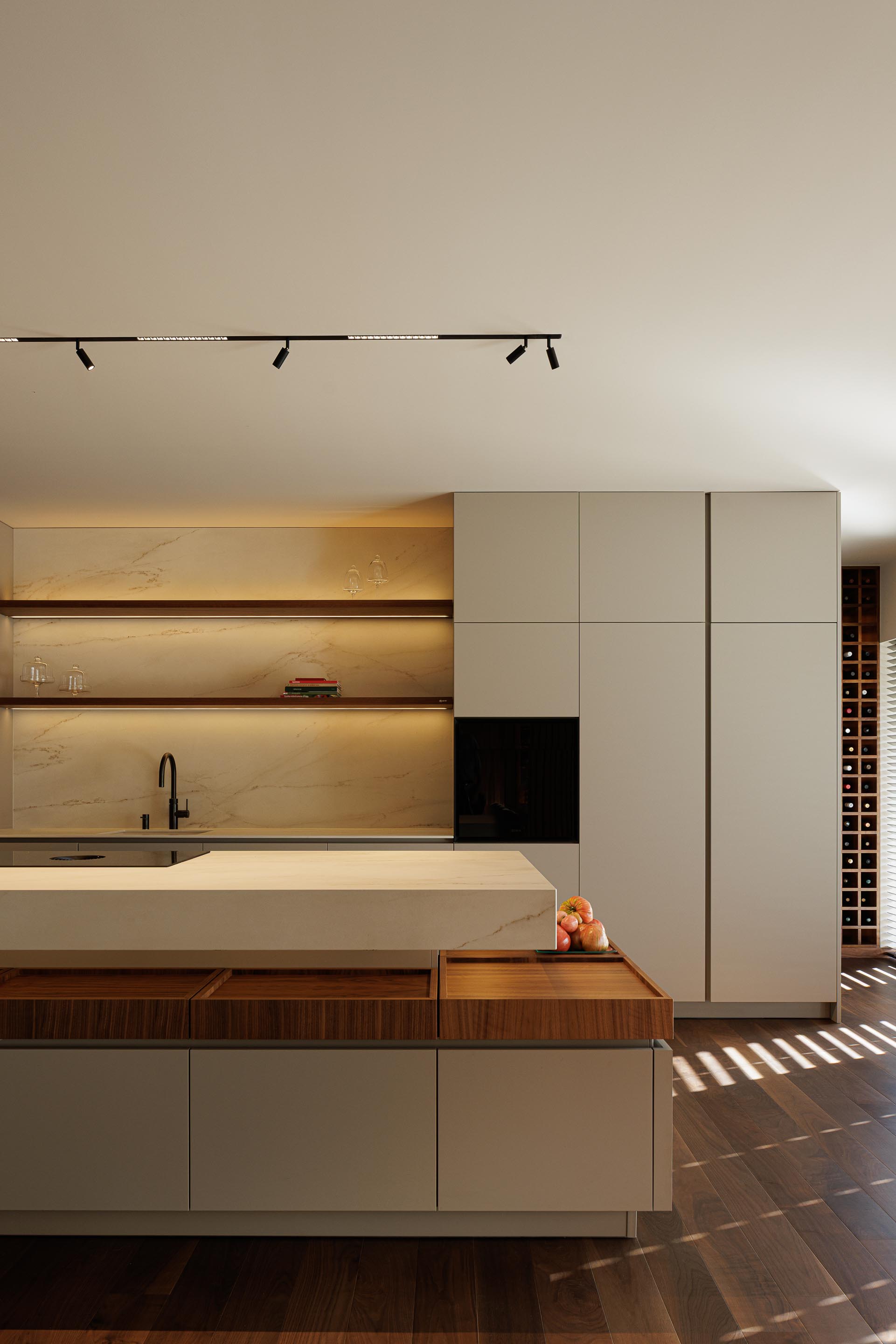 Cozinha: Ilha central com bancada em mármore branco, armários brancos e garrafeira ao fundo. — Casa do Engenho arquitetura silverline em Vila Nova de Gaia