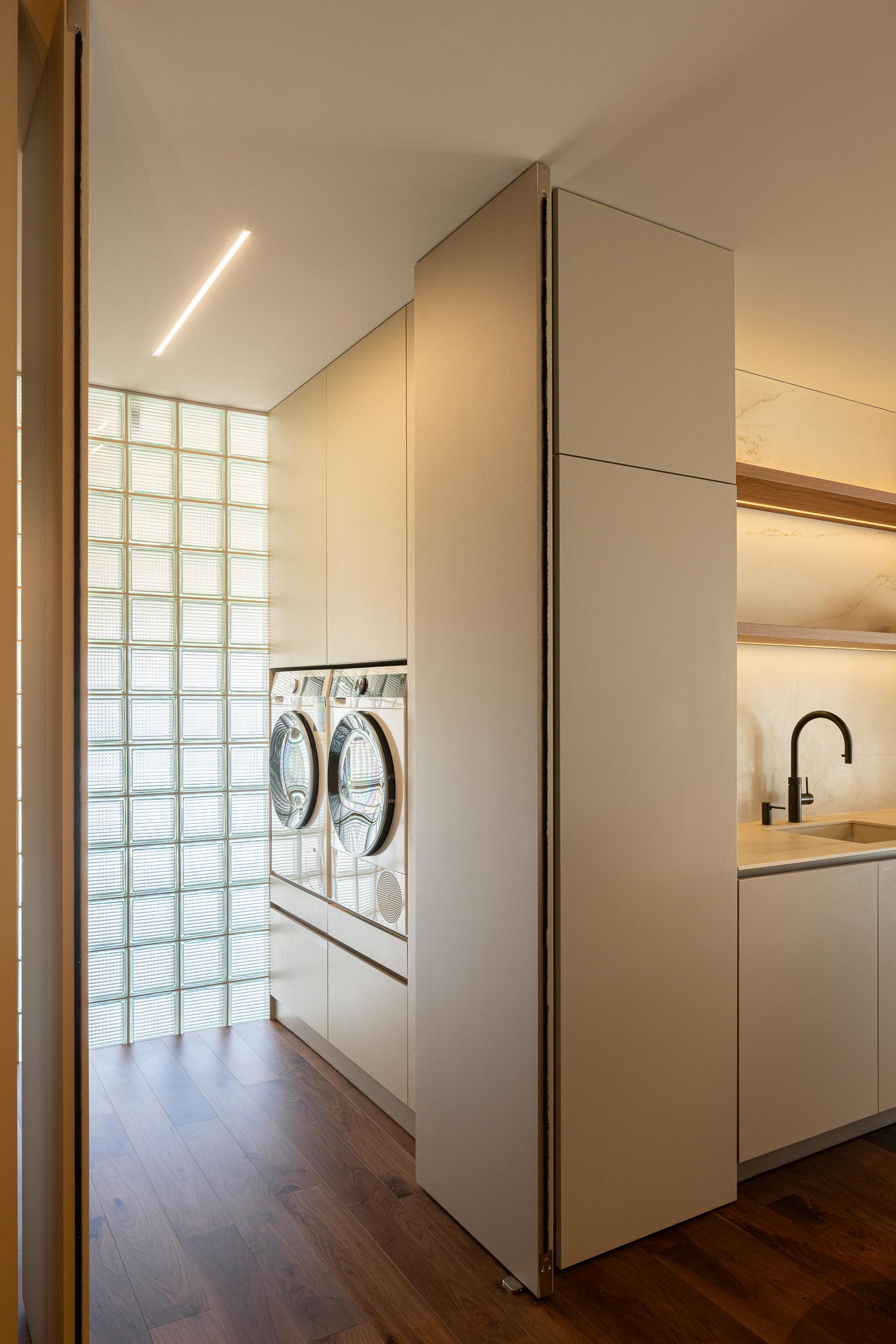 Lavandaria: Máquinas de lavar e secar roupa, parede de blocos de vidro e bancada com lavatório. — Casa do Engenho arquitetura silverline em Vila Nova de Gaia