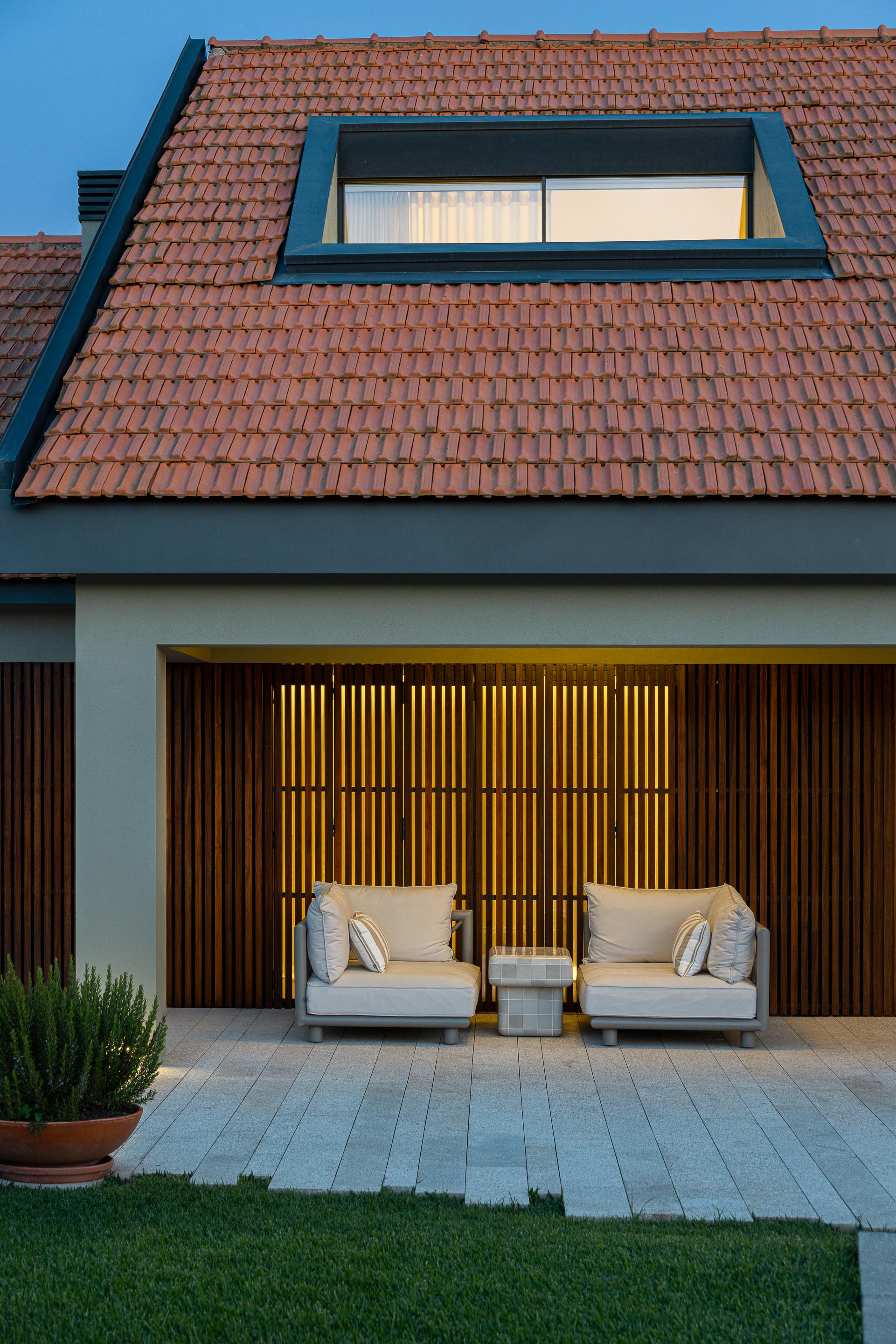 Exterior: Fachada da casa com porta em ripas de madeira, sofás de exterior e iluminação noturna. — Casa do Engenho arquitetura silverline em Vila Nova de Gaia
