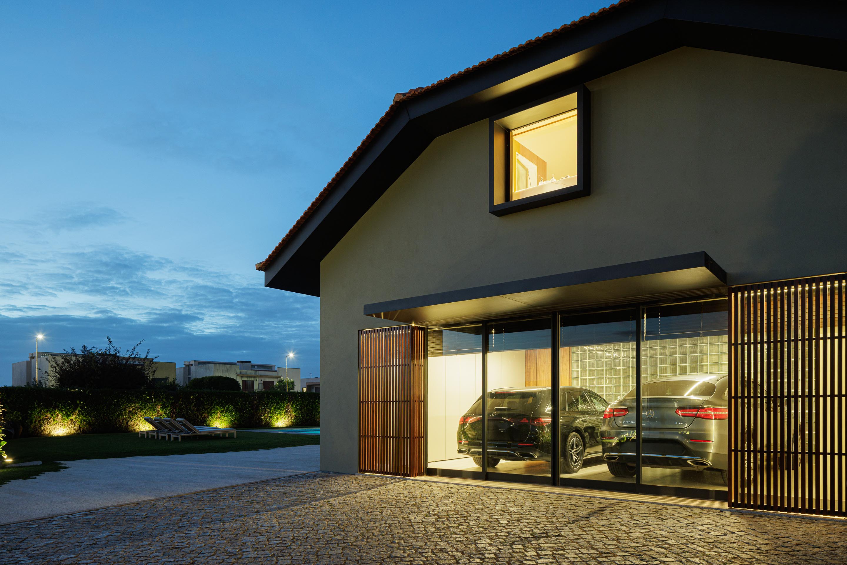 Exterior: Garagem com porta em ripas de madeira, carros estacionados e iluminação exterior. — Casa do Engenho arquitetura silverline em Vila Nova de Gaia