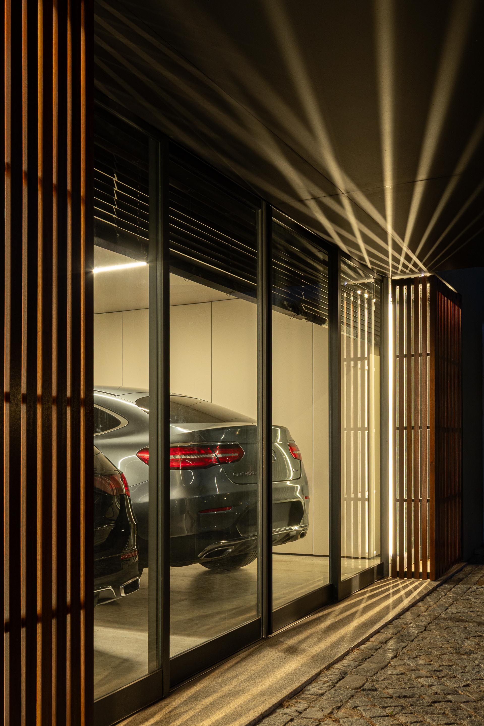 Garagem: Detalhe da porta em ripas de madeira, carros estacionados e iluminação interior. — Casa do Engenho arquitetura silverline em Vila Nova de Gaia