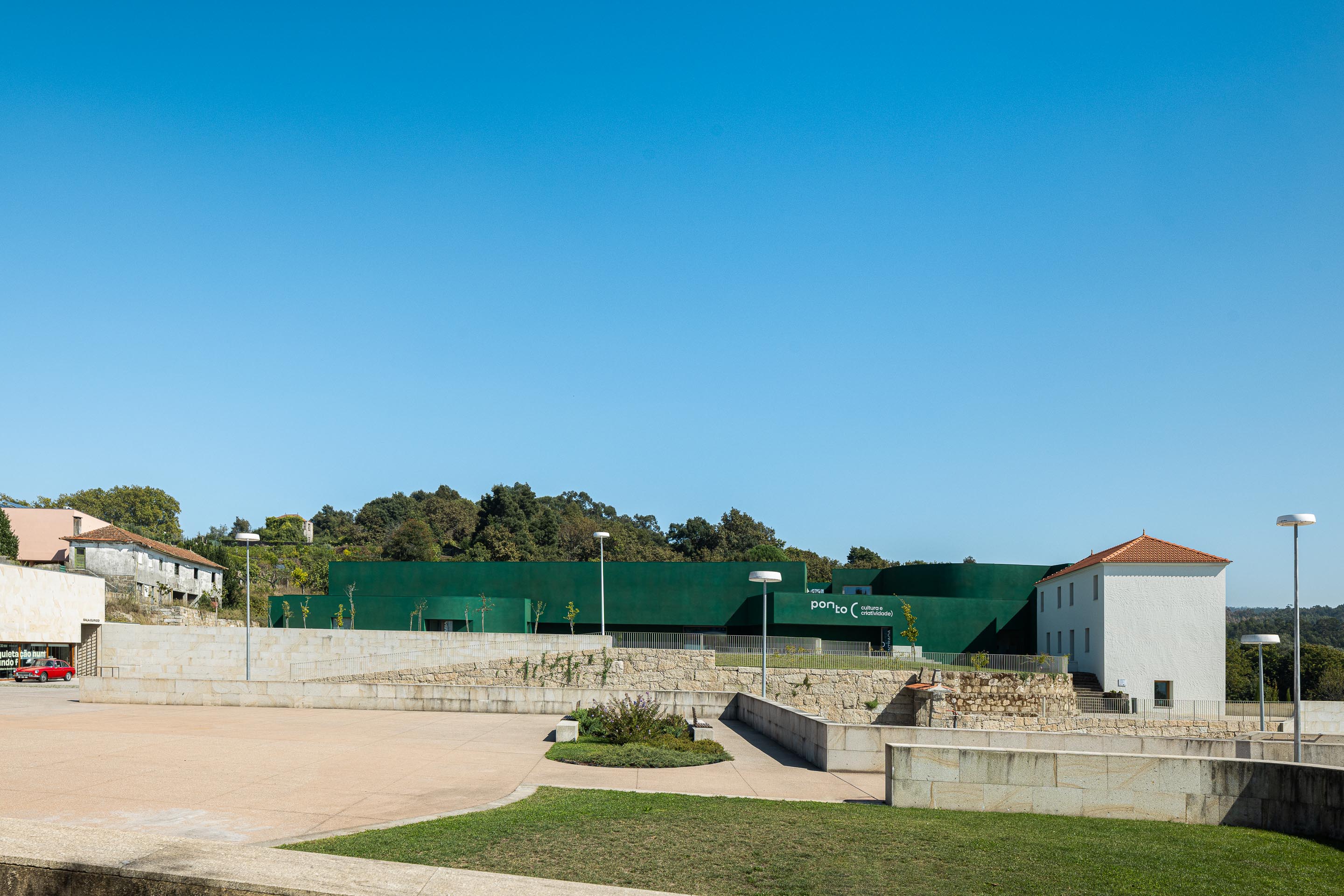 Fachada: Vista ampla do edifício "Ponto C" em verde, com relvado e edifícios antigos em redor. — Ponto C - Cultura e Criatividade arquitetura Galeria Gabinete em Penafiel
