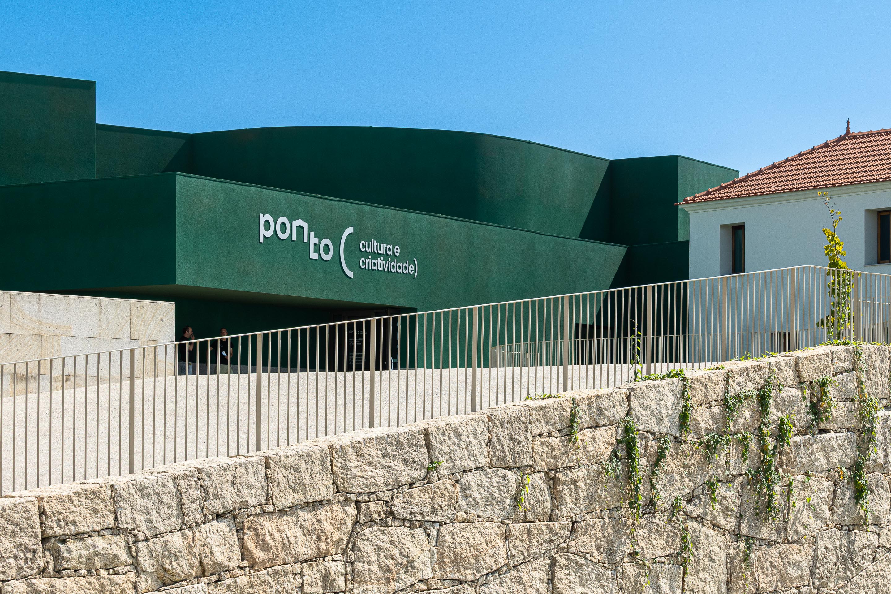 Fachada: Detalhe da fachada verde do "Ponto C" com o nome do projeto e muro de pedra. — Ponto C - Cultura e Criatividade arquitetura Galeria Gabinete em Penafiel