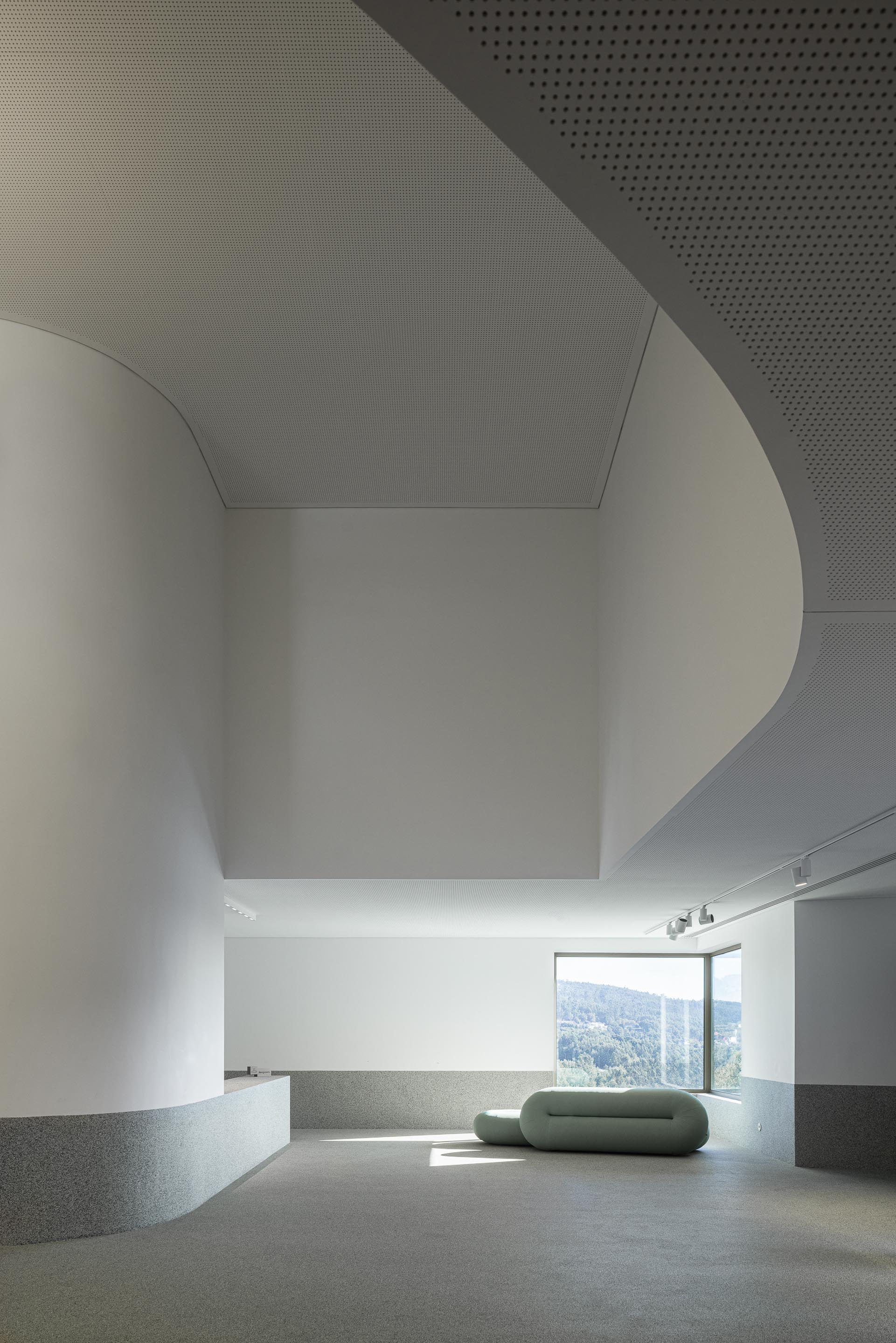 Hall de entrada: Detalhe do teto curvo e parede branca, com zona de estar e janela panorâmica. — Ponto C - Cultura e Criatividade arquitetura Galeria Gabinete em Penafiel