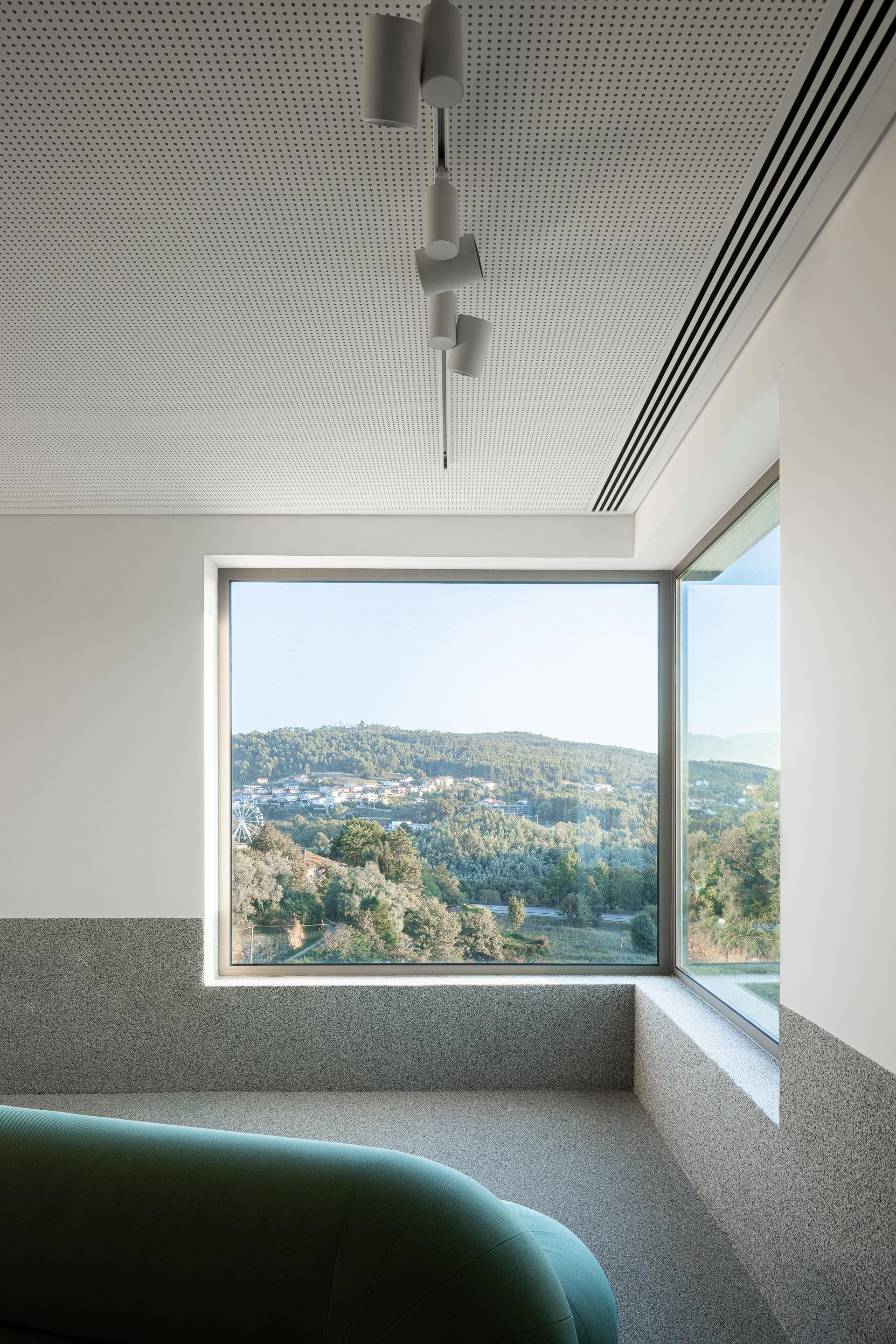 Hall de entrada: Canto com janela, teto perfurado e candeeiro suspenso minimalista. — Ponto C - Cultura e Criatividade arquitetura Galeria Gabinete em Penafiel