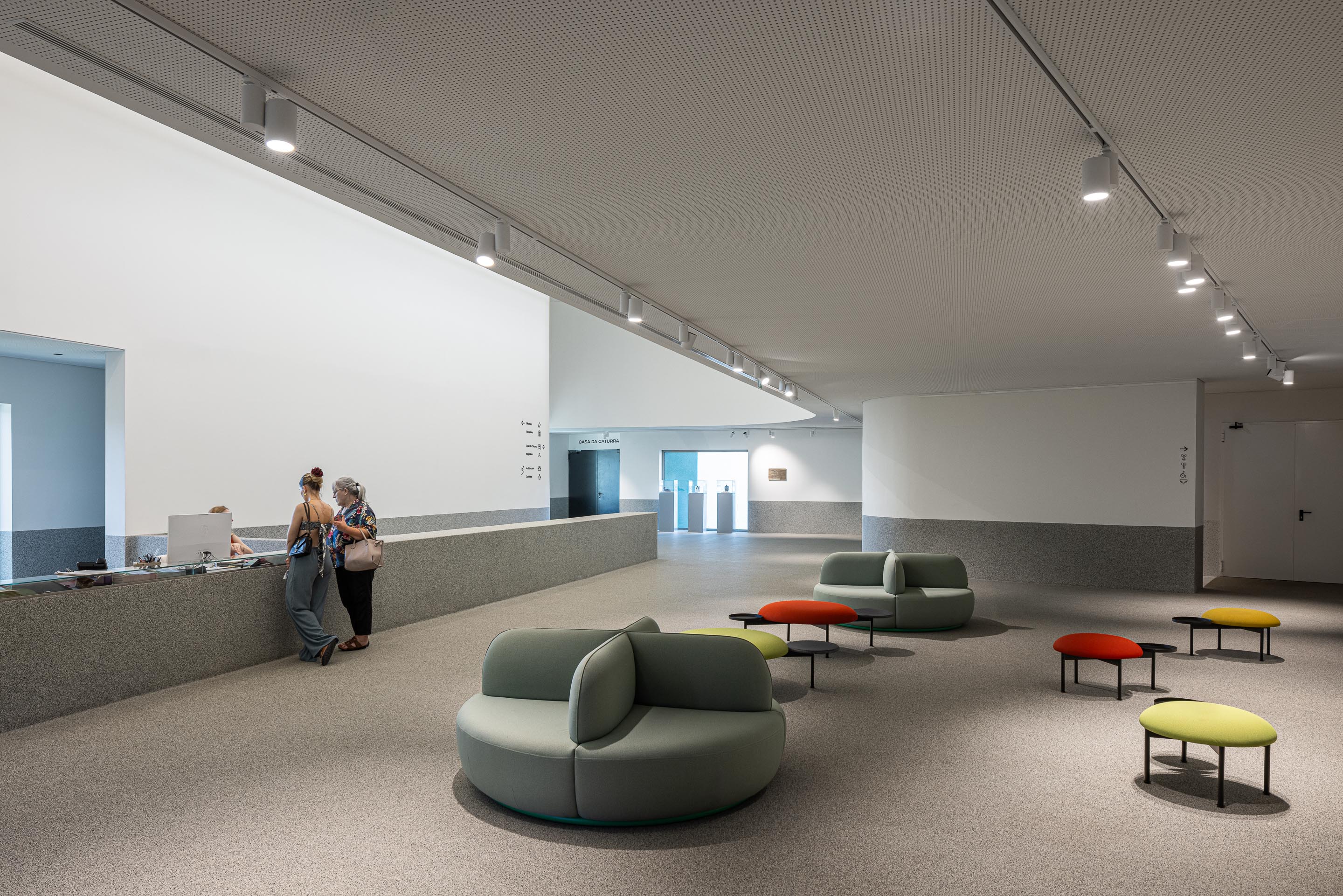 Hall de entrada: Balcão de receção, sofás circulares e iluminação embutida no teto. — Ponto C - Cultura e Criatividade arquitetura Galeria Gabinete em Penafiel