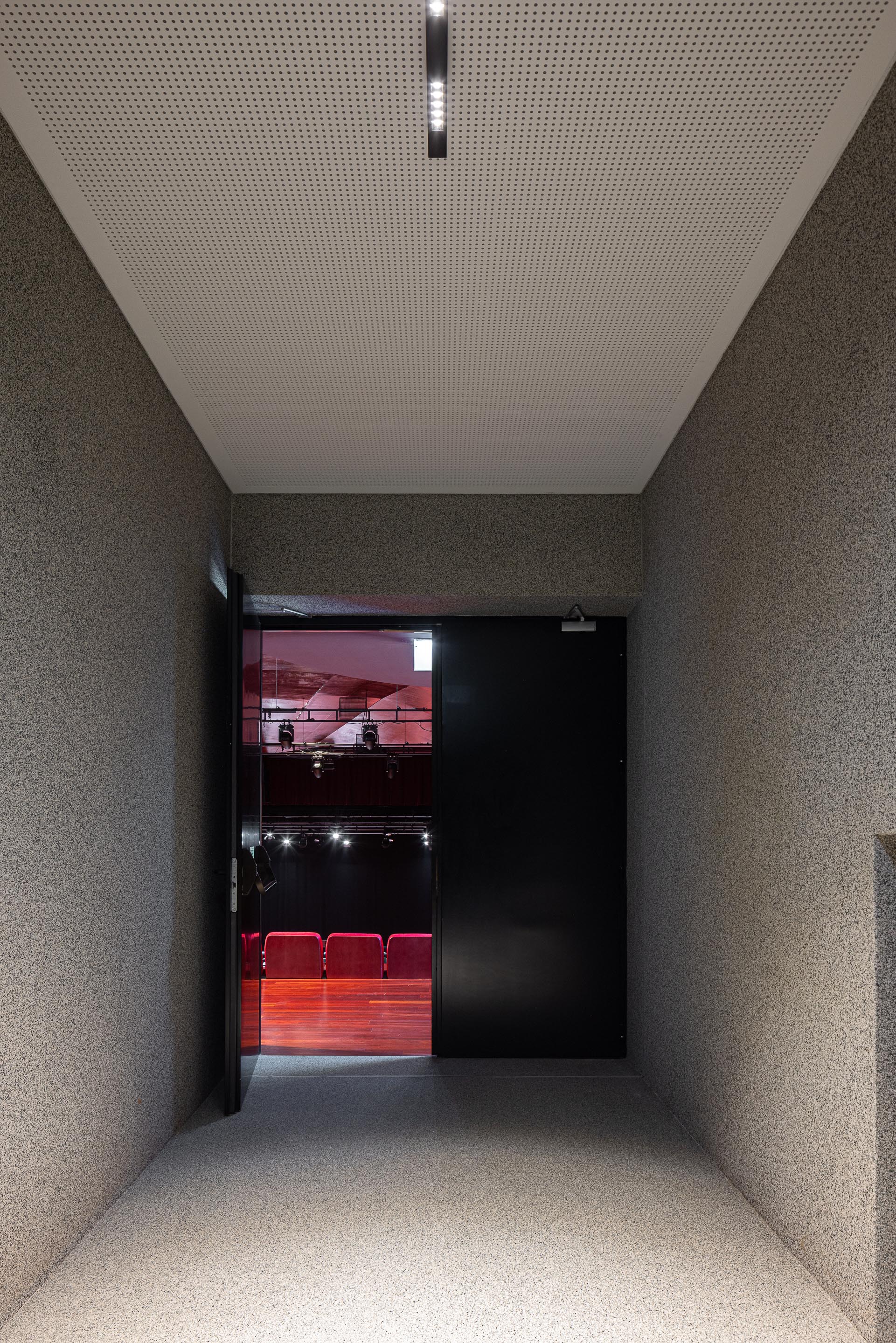 Corredor: Acesso ao auditório, com paredes texturadas e porta preta entreaberta. — Ponto C - Cultura e Criatividade arquitetura Galeria Gabinete em Penafiel