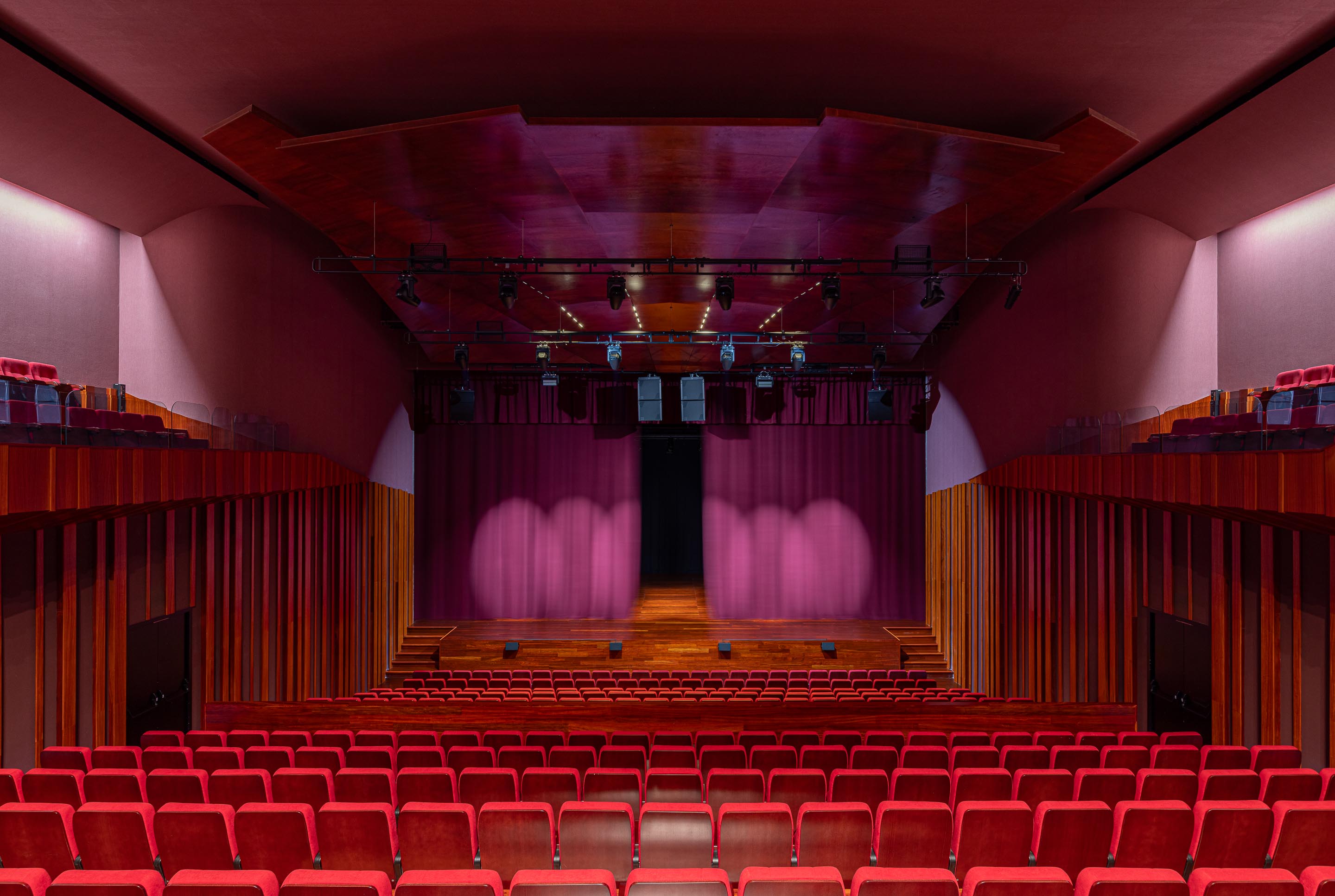 Auditório: Vista geral do auditório com cadeiras vermelhas, palco em madeira e cortinas. — Ponto C - Cultura e Criatividade arquitetura Galeria Gabinete em Penafiel