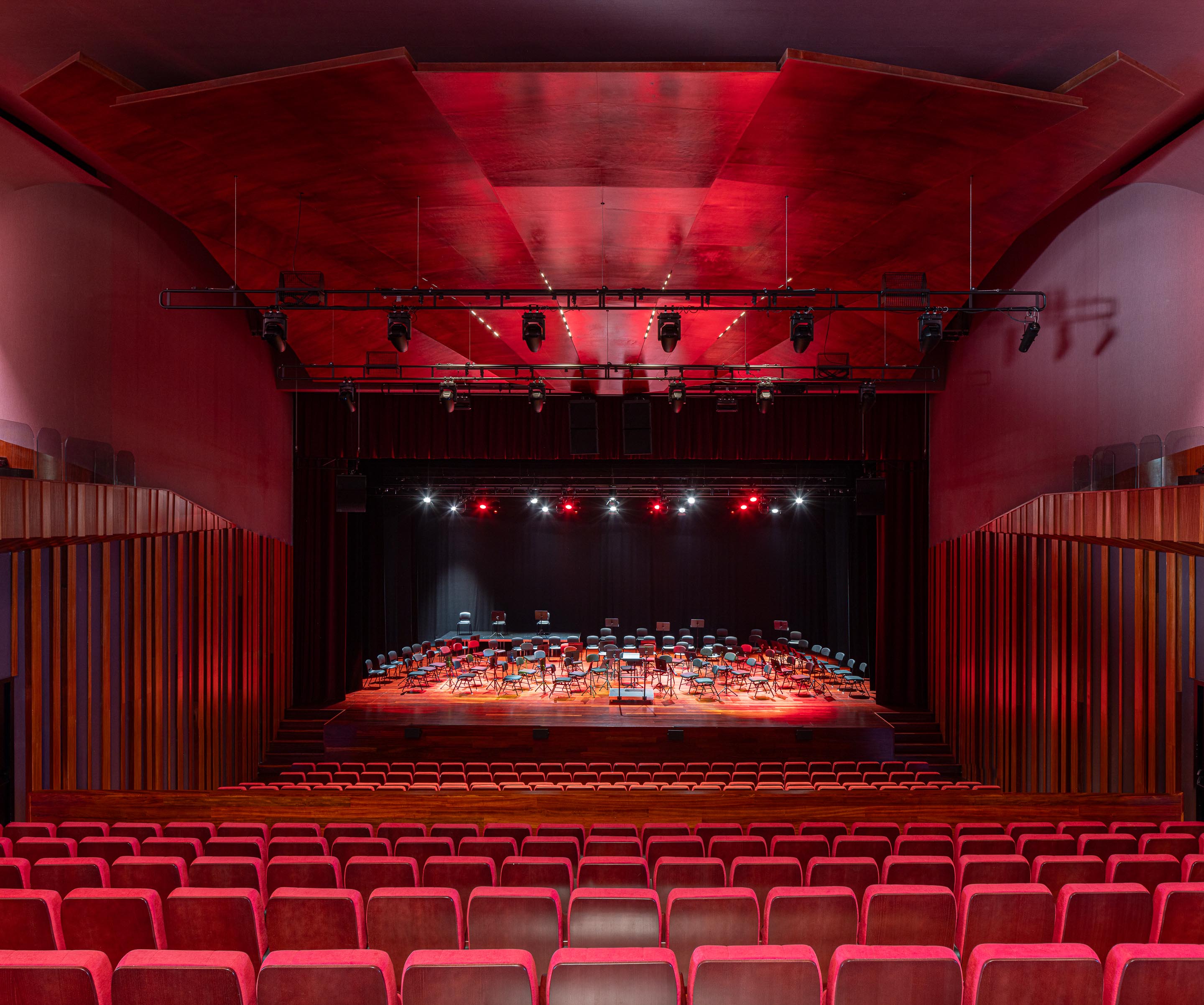 Auditório: Palco com cadeiras e iluminação, visto da plateia com cadeiras vermelhas. — Ponto C - Cultura e Criatividade arquitetura Galeria Gabinete em Penafiel