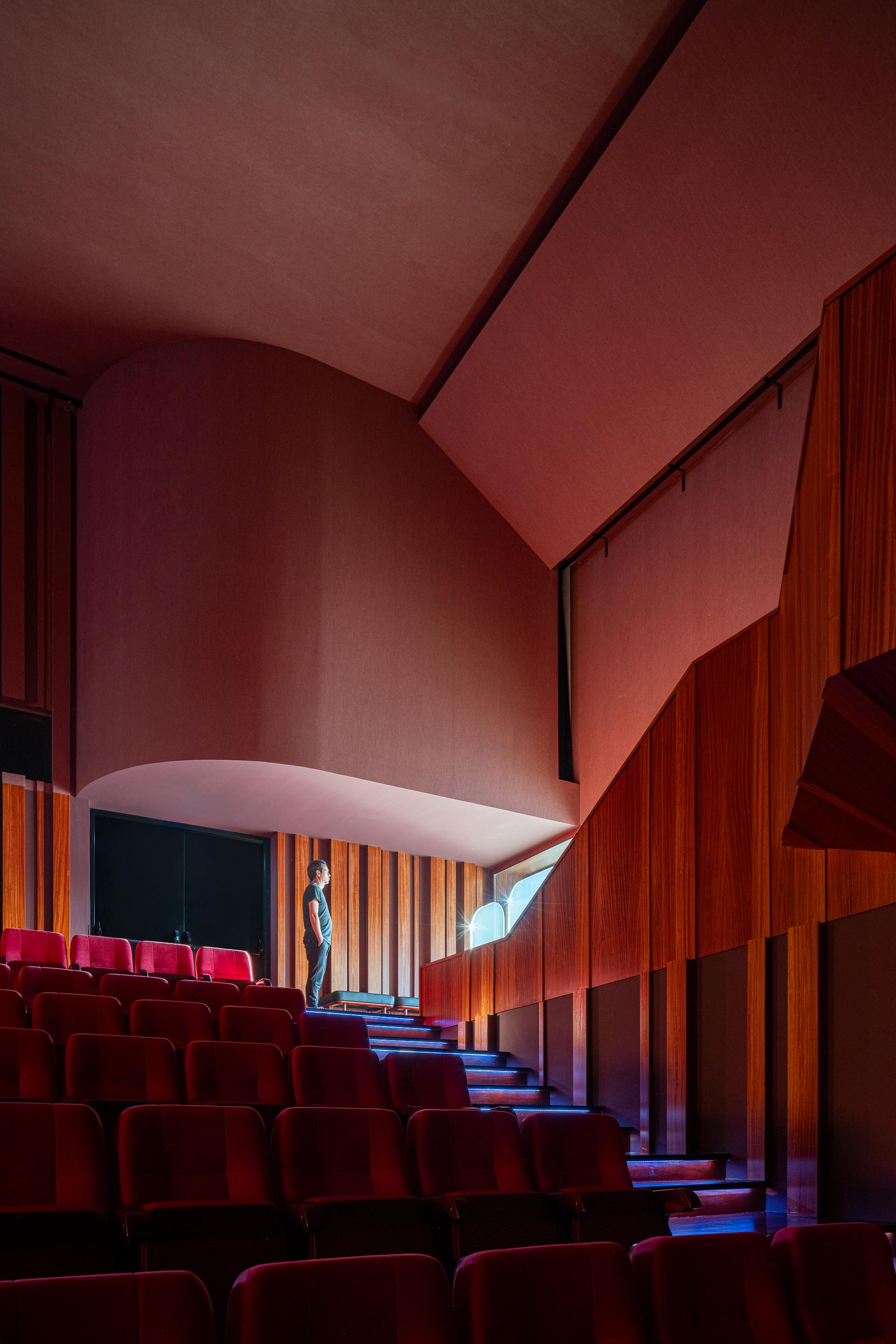 Auditório: Escadas laterais com revestimento em madeira e cadeiras vermelhas. — Ponto C - Cultura e Criatividade arquitetura Galeria Gabinete em Penafiel