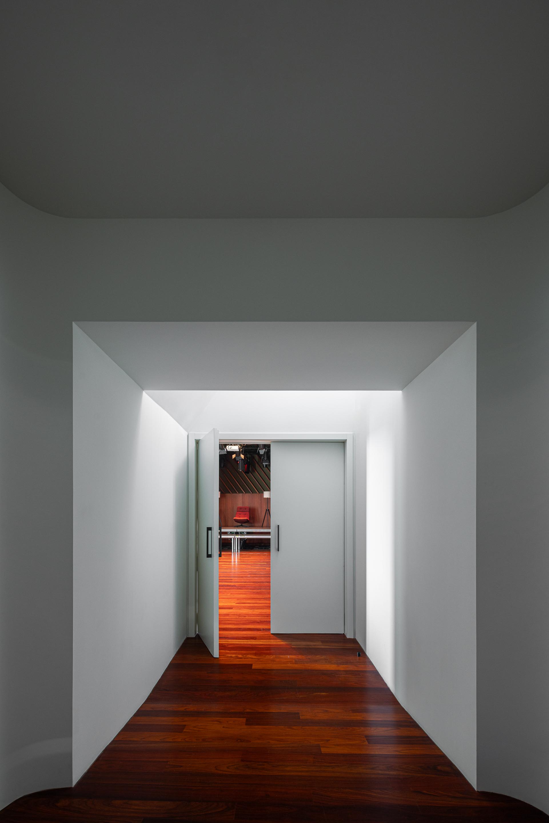 Corredor: Acesso ao palco, com pavimento em madeira e paredes brancas. — Ponto C - Cultura e Criatividade arquitetura Galeria Gabinete em Penafiel