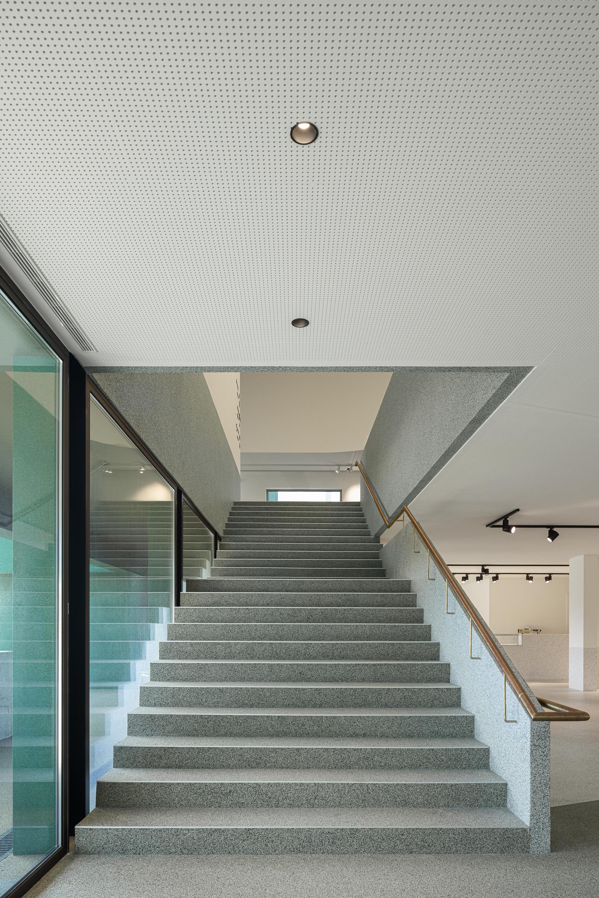 Escadas: Vista ascendente das escadas em granito, com iluminação e guarda em vidro. — Ponto C - Cultura e Criatividade arquitetura Galeria Gabinete em Penafiel