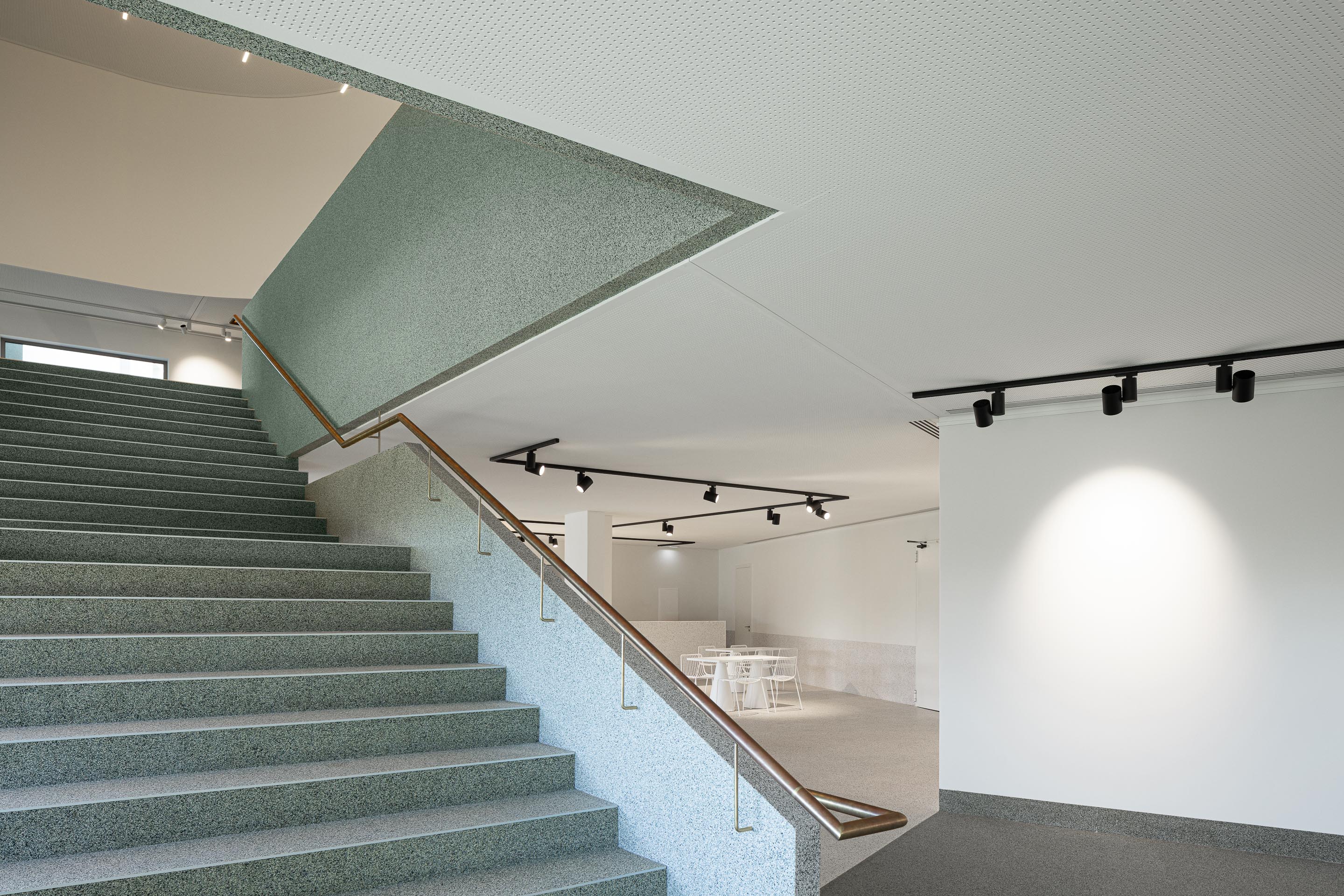Escadas: Escadas em granito com corrimão em metal dourado e iluminação direcionada. — Ponto C - Cultura e Criatividade arquitetura Galeria Gabinete em Penafiel