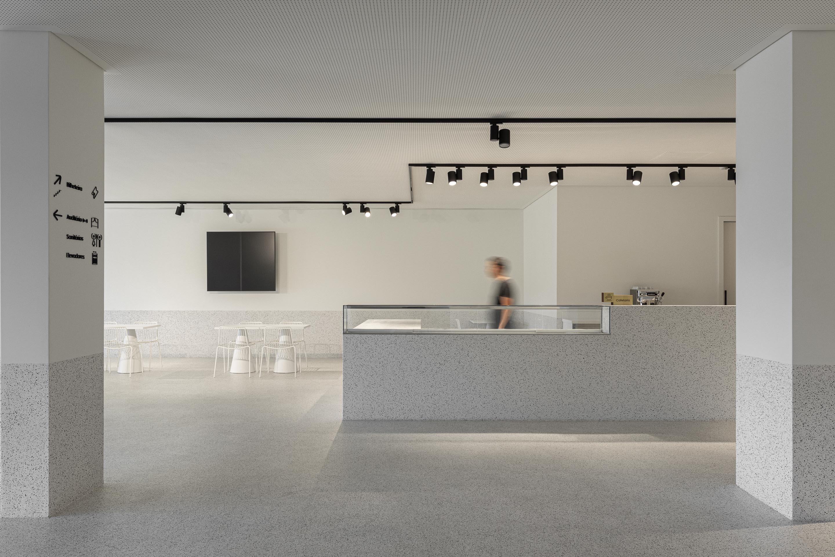 Cafetaria: Balcão com detalhes em granito, mesas e cadeiras brancas e iluminação embutida. — Ponto C - Cultura e Criatividade arquitetura Galeria Gabinete em Penafiel