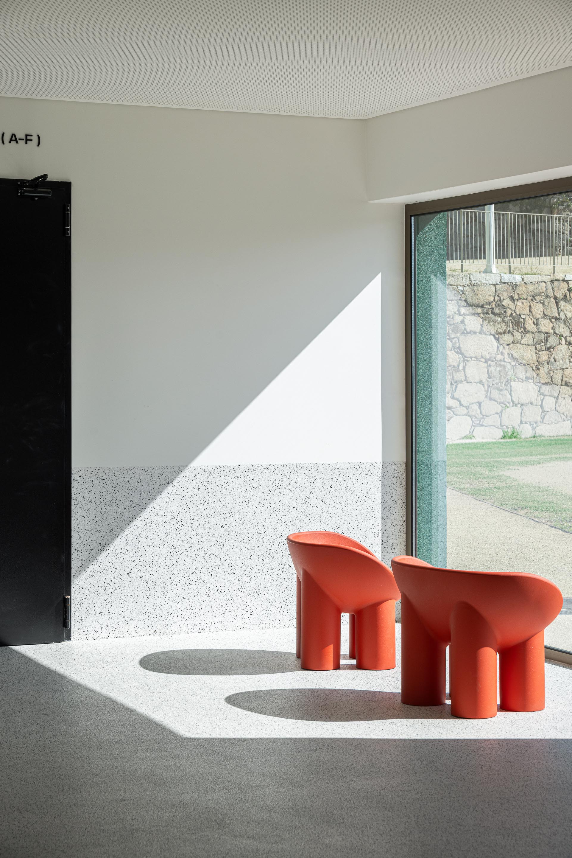Espaço de estar: Cadeiras laranjas de design moderno junto a uma janela com vista para o exterior. — Ponto C - Cultura e Criatividade arquitetura Galeria Gabinete em Penafiel