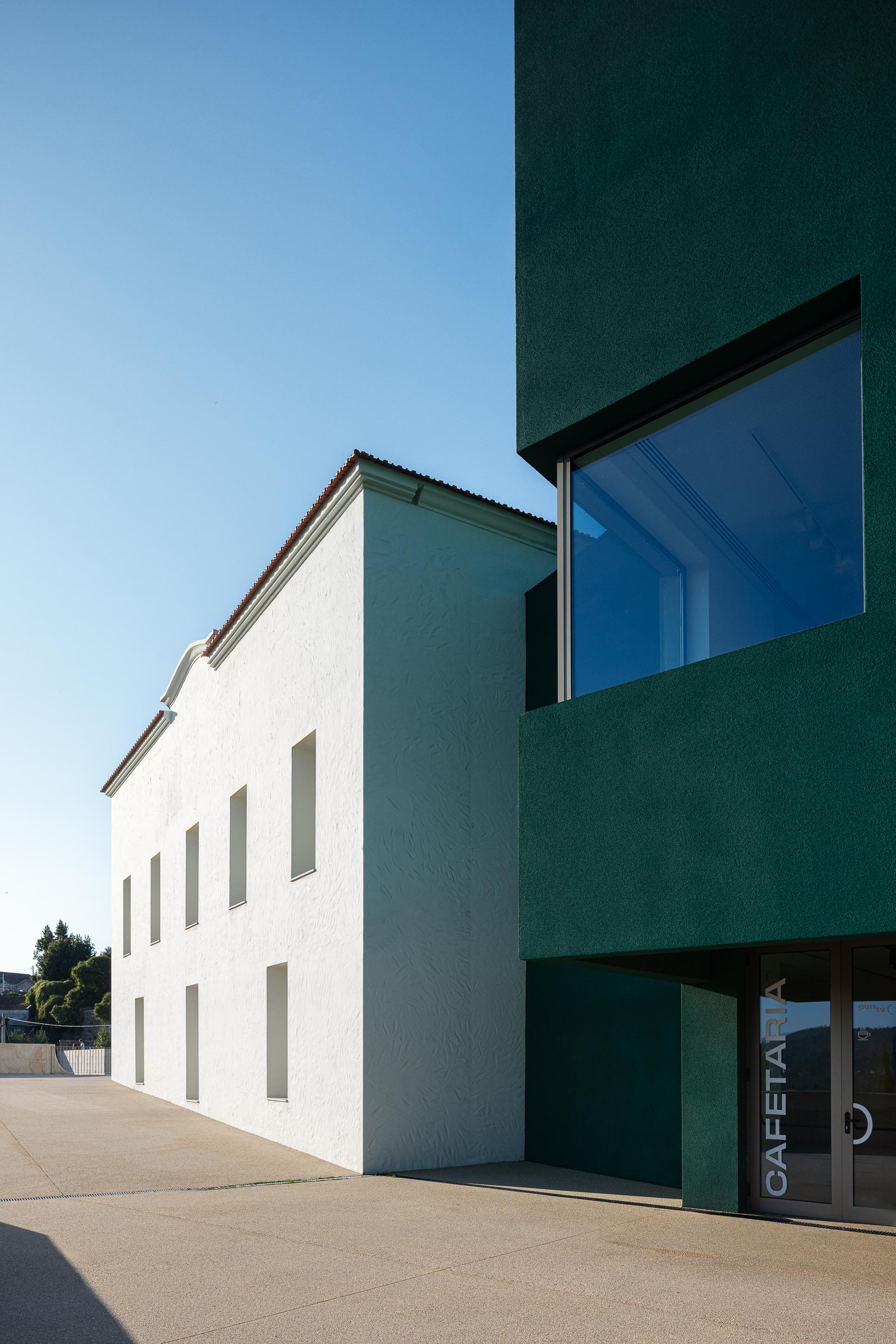 Exterior: Edifício branco com janelas, junto ao edifício verde da cafetaria. — Ponto C - Cultura e Criatividade arquitetura Galeria Gabinete em Penafiel
