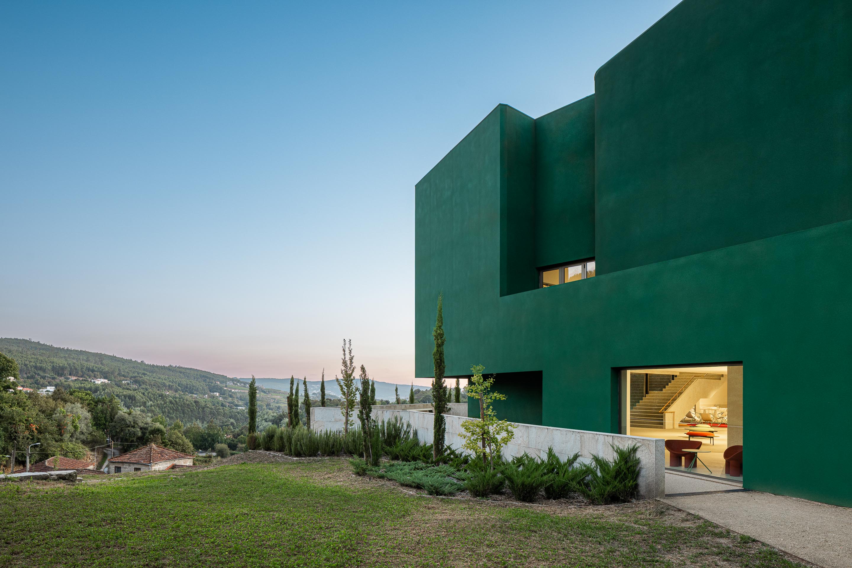 Exterior: Edifício verde com janelas e vegetação, visto do jardim. — Ponto C - Cultura e Criatividade arquitetura Galeria Gabinete em Penafiel
