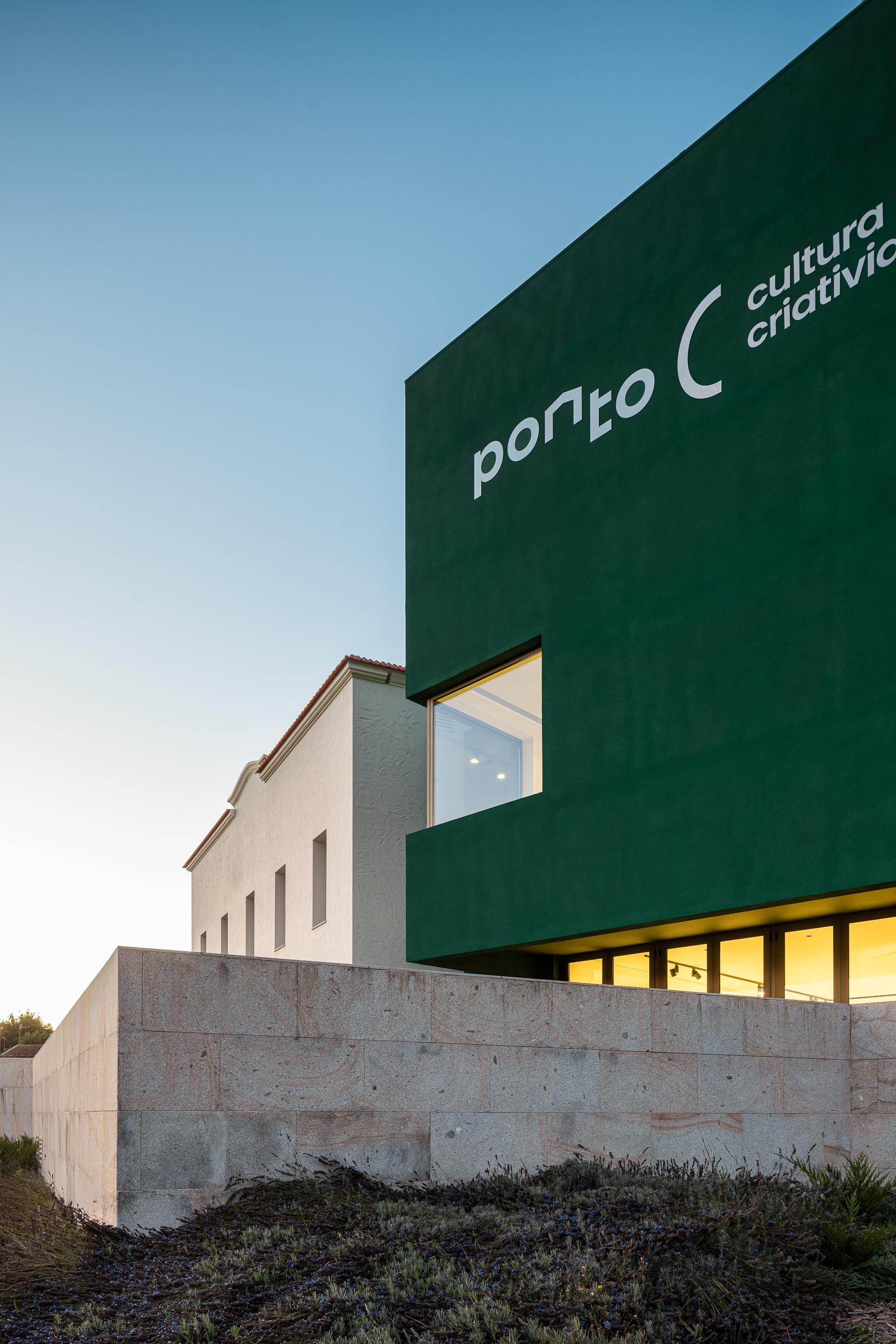Fachada: Edifício verde com o nome "Ponto C" e edifício branco ao lado, com muro de pedra. — Ponto C - Cultura e Criatividade arquitetura Galeria Gabinete em Penafiel