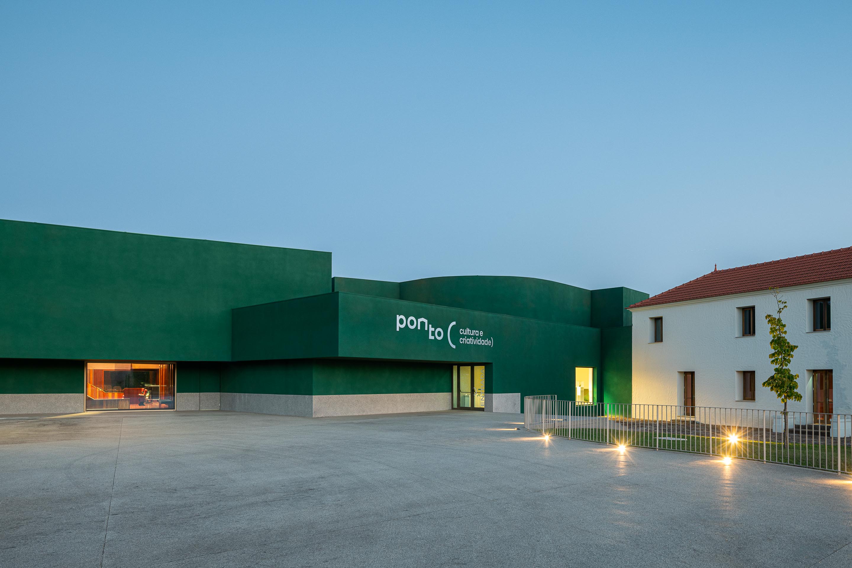 Fachada: Vista noturna do edifício verde "Ponto C" com iluminação e edifício branco ao lado. — Ponto C - Cultura e Criatividade arquitetura Galeria Gabinete em Penafiel