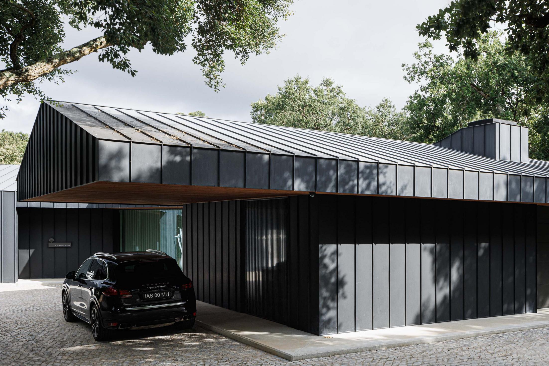 Exterior: Vista da casa com revestimento metálico preto, telhado inclinado, alpendre em madeira e automóvel estacionado. — CC House – Quinta dos Carvalhos arquitetura Inception Architects Studio em Leiria
