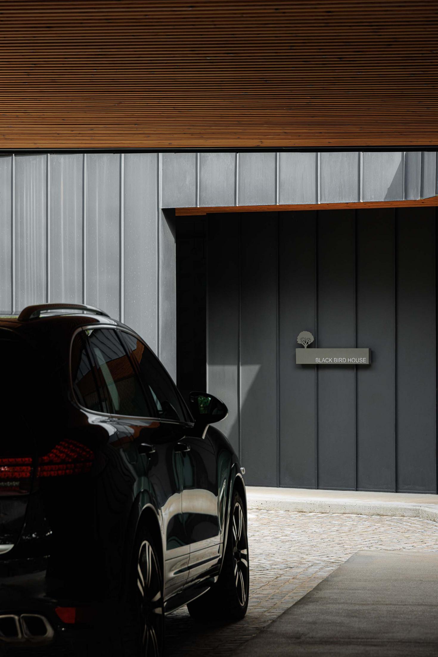 Exterior: Vista lateral da casa com automóvel estacionado e placa com o nome "Black Bird House". — CC House – Quinta dos Carvalhos arquitetura Inception Architects Studio em Leiria