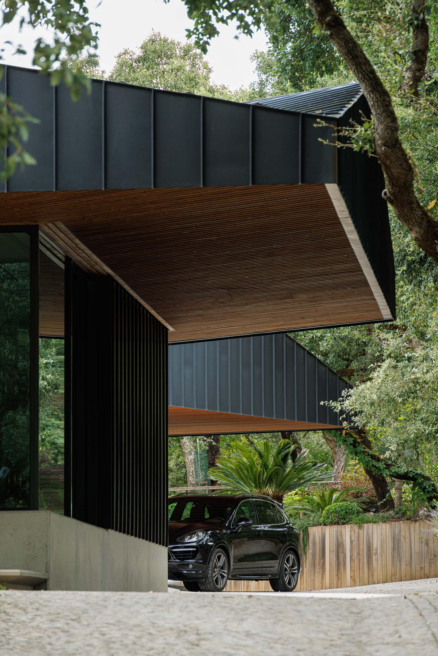 Exterior: Vista da casa com revestimento metálico preto, alpendre em madeira e automóvel estacionado. — CC House – Quinta dos Carvalhos arquitetura Inception Architects Studio em Leiria