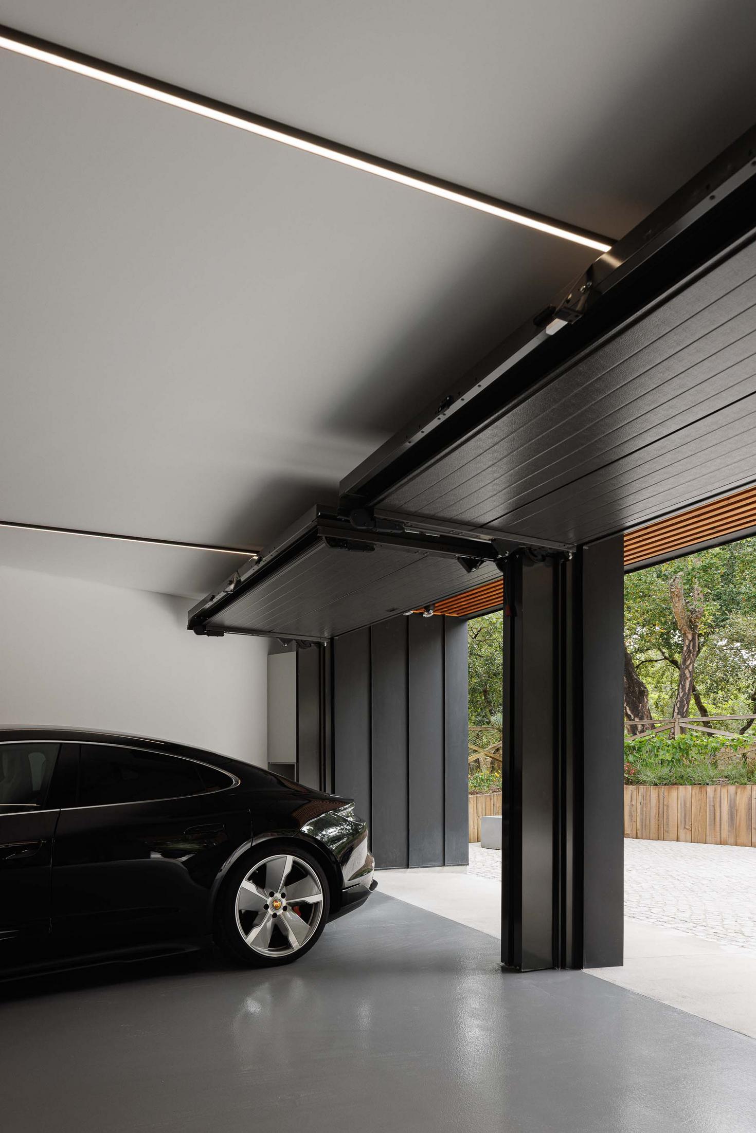 Garagem: Automóvel preto estacionado na garagem com porta seccionada aberta e teto em madeira. — CC House – Quinta dos Carvalhos arquitetura Inception Architects Studio em Leiria