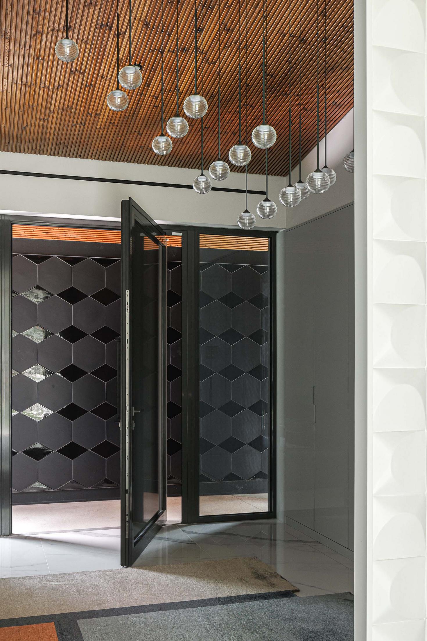Hall de entrada: Porta de entrada com padrão geométrico, candeeiros suspensos e parede com revestimento branco texturado. — CC House – Quinta dos Carvalhos arquitetura Inception Architects Studio em Leiria
