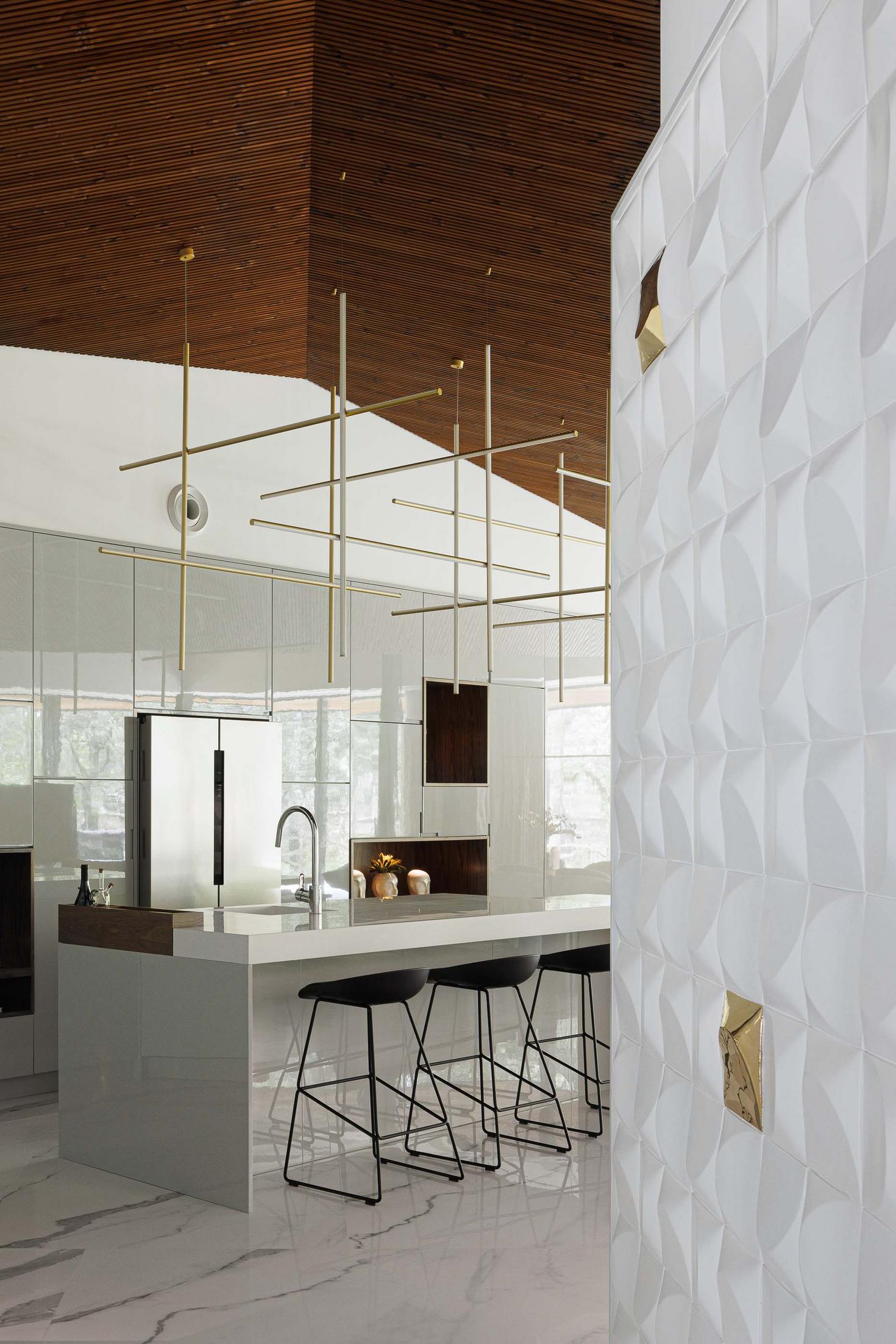 Cozinha: Ilha central com bancada branca, cadeiras altas pretas, candeeiros suspensos e parede com revestimento branco texturado. — CC House – Quinta dos Carvalhos arquitetura Inception Architects Studio em Leiria