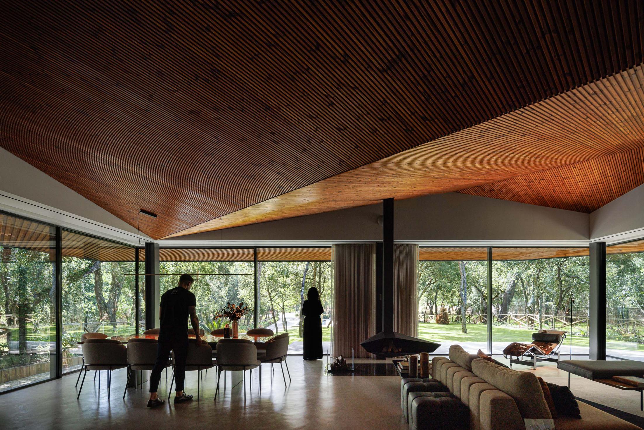 Sala de estar/Jantar: Espaço amplo com sala de estar, mesa de jantar, lareira suspensa e grandes janelas com vista para o jardim. — CC House – Quinta dos Carvalhos arquitetura Inception Architects Studio em Leiria