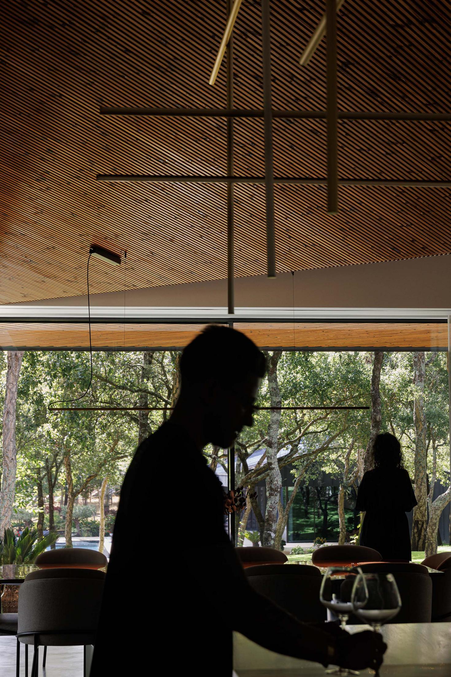 Sala de jantar: Silhuetas de pessoas na sala de jantar com mesa, cadeiras e vista para o jardim. — CC House – Quinta dos Carvalhos arquitetura Inception Architects Studio em Leiria