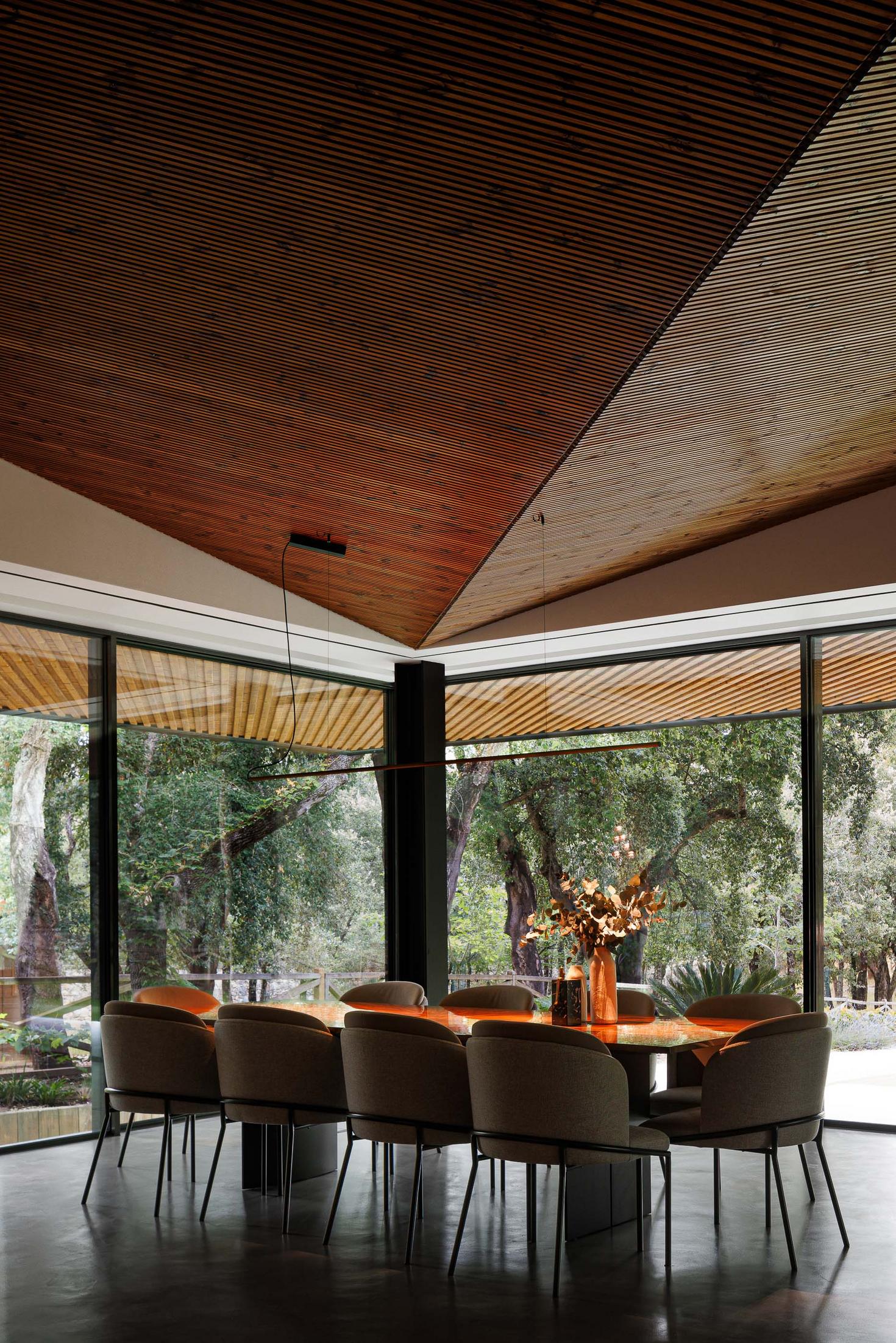 Sala de jantar: Mesa de jantar com cadeiras, candeeiro suspenso linear e vista para o jardim. — CC House – Quinta dos Carvalhos arquitetura Inception Architects Studio em Leiria