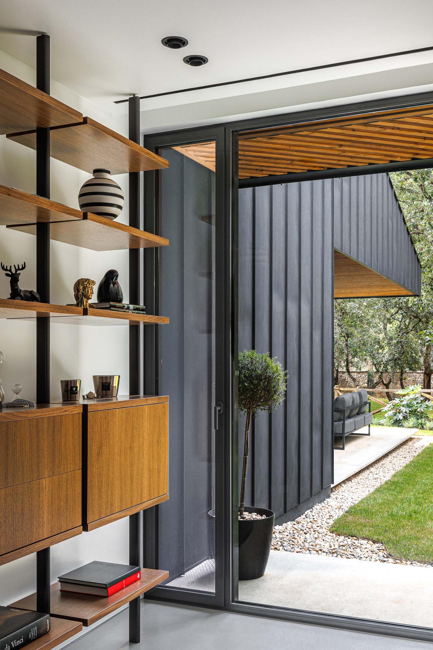 Escritório: Estantes em madeira com objetos decorativos e vista para o exterior. — CC House – Quinta dos Carvalhos arquitetura Inception Architects Studio em Leiria