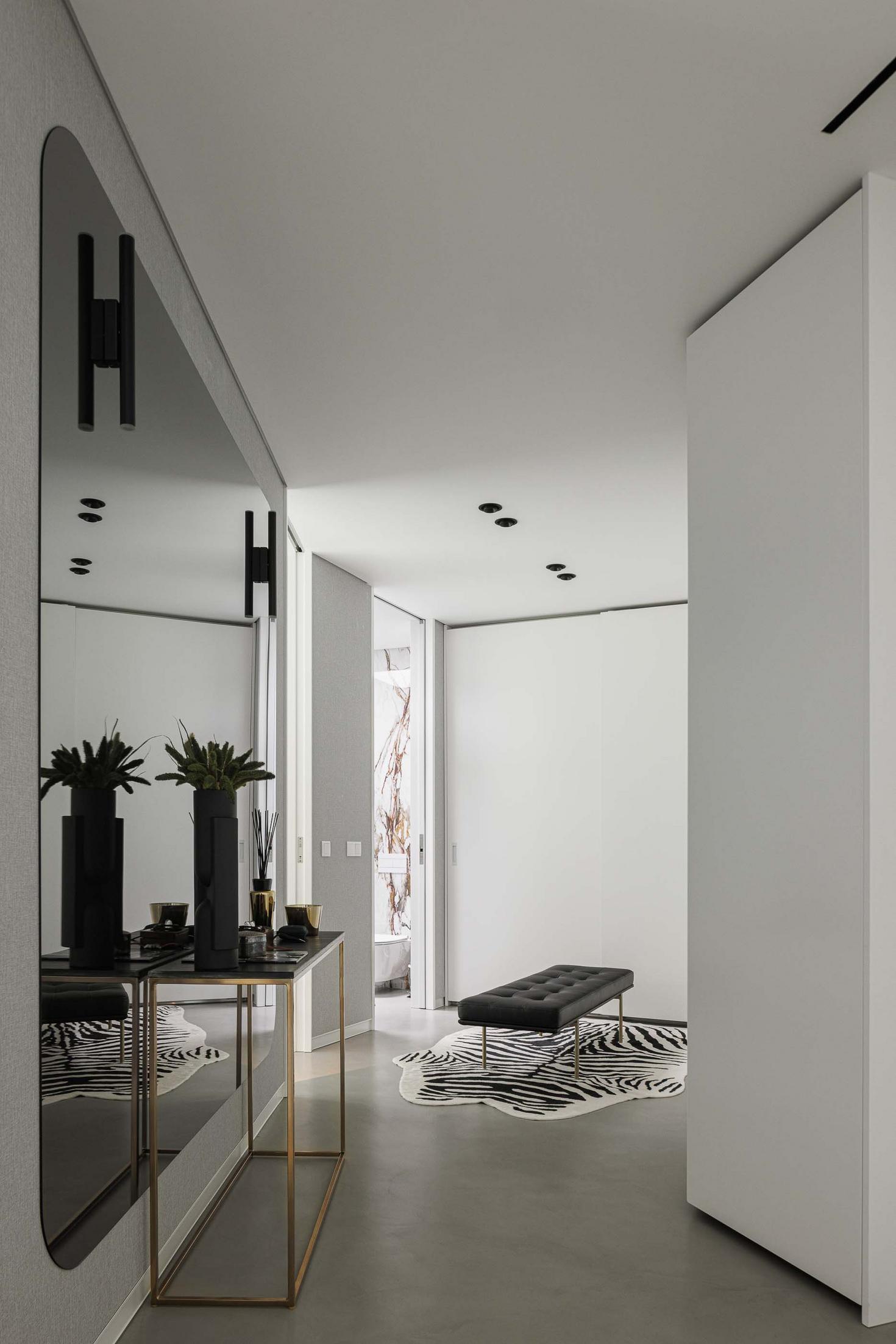 Hall de entrada: Espelho amplo, consola dourada, banco com padrão zebra e pavimento em cimento afagado. — CC House – Quinta dos Carvalhos arquitetura Inception Architects Studio em Leiria
