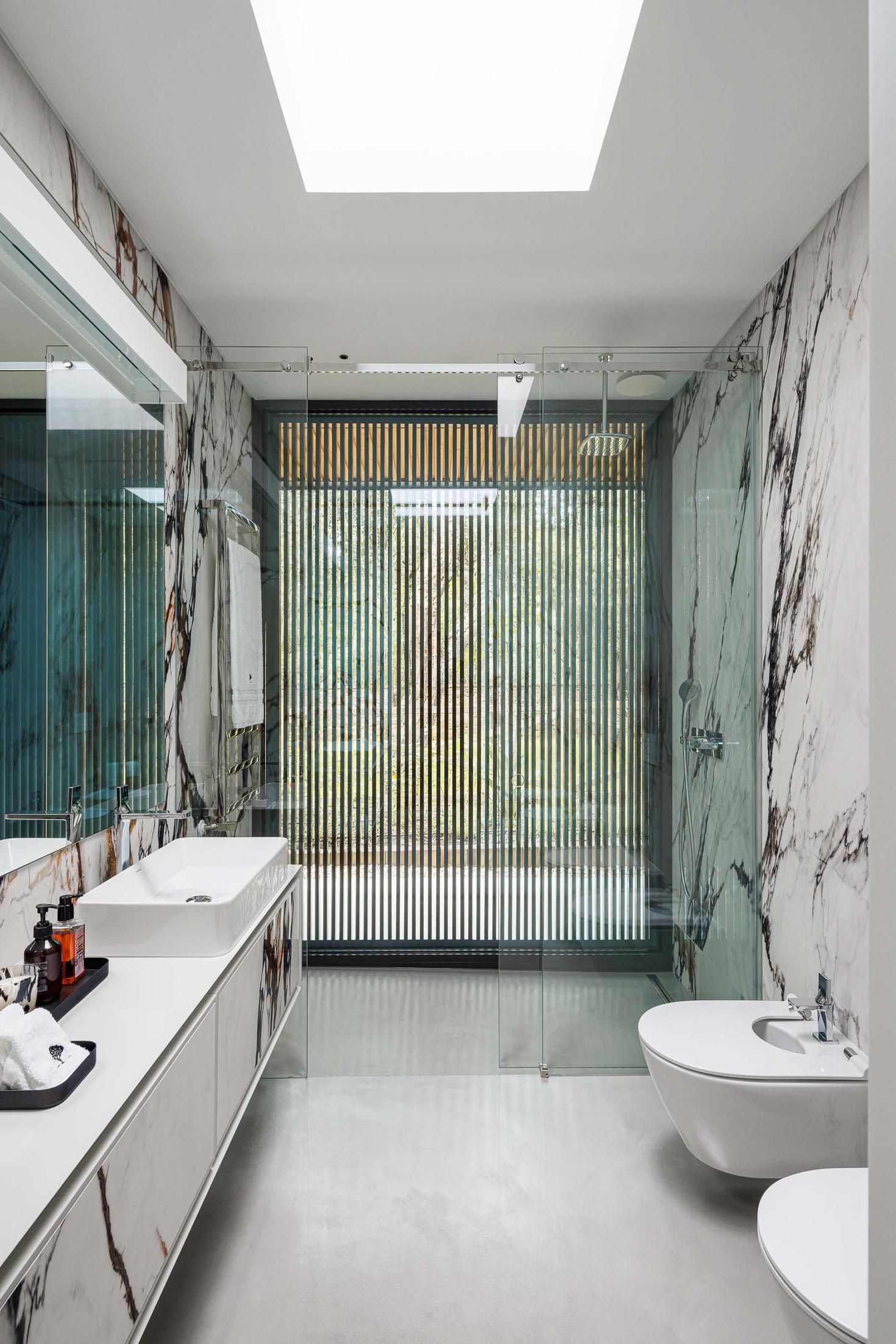 Casa de banho: Revestimento em mármore branco com veios castanhos, cabine de duche e lavatório branco. — CC House – Quinta dos Carvalhos arquitetura Inception Architects Studio em Leiria