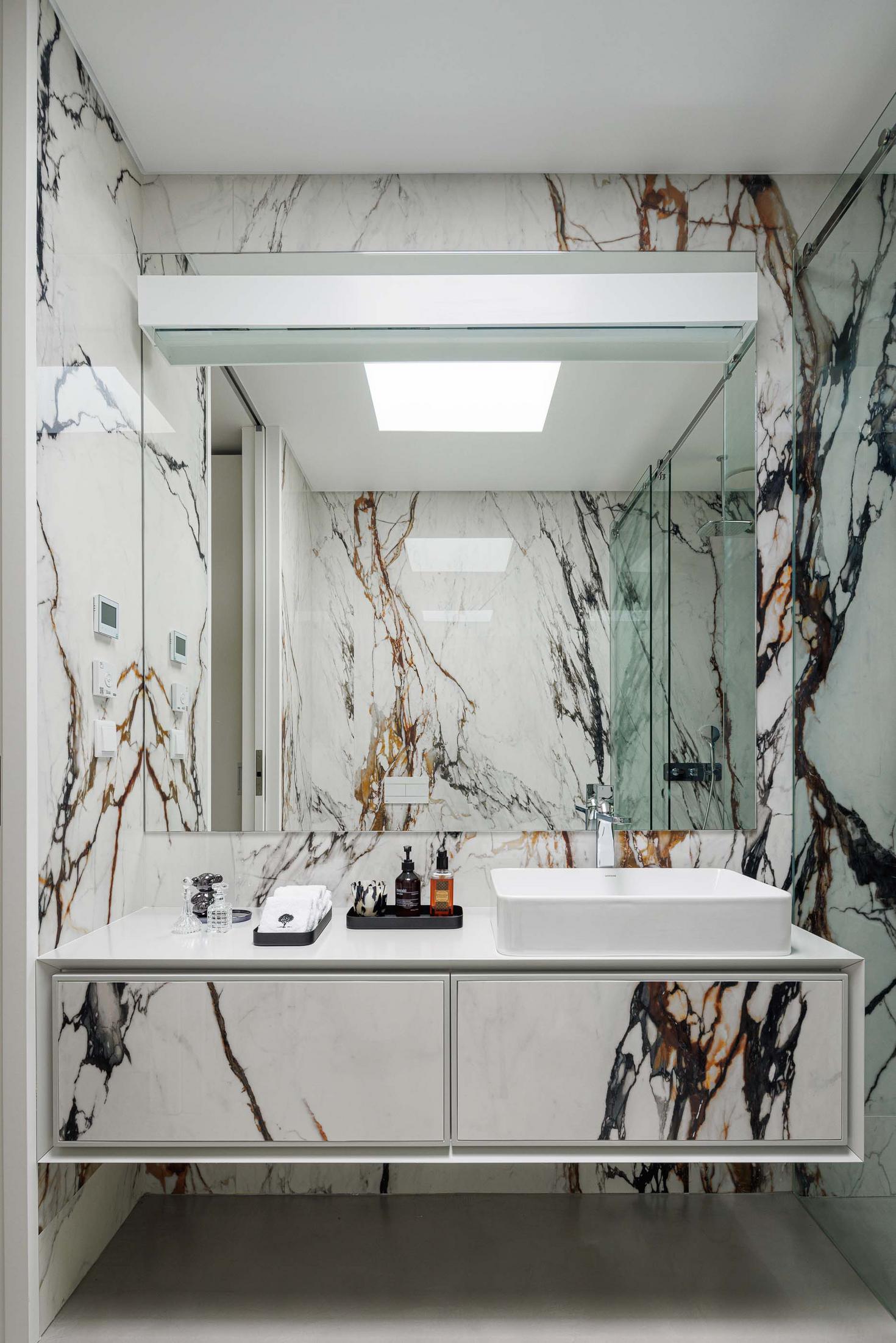 Casa de banho: Revestimento em mármore branco com veios castanhos, lavatório branco e espelho amplo. — CC House – Quinta dos Carvalhos arquitetura Inception Architects Studio em Leiria