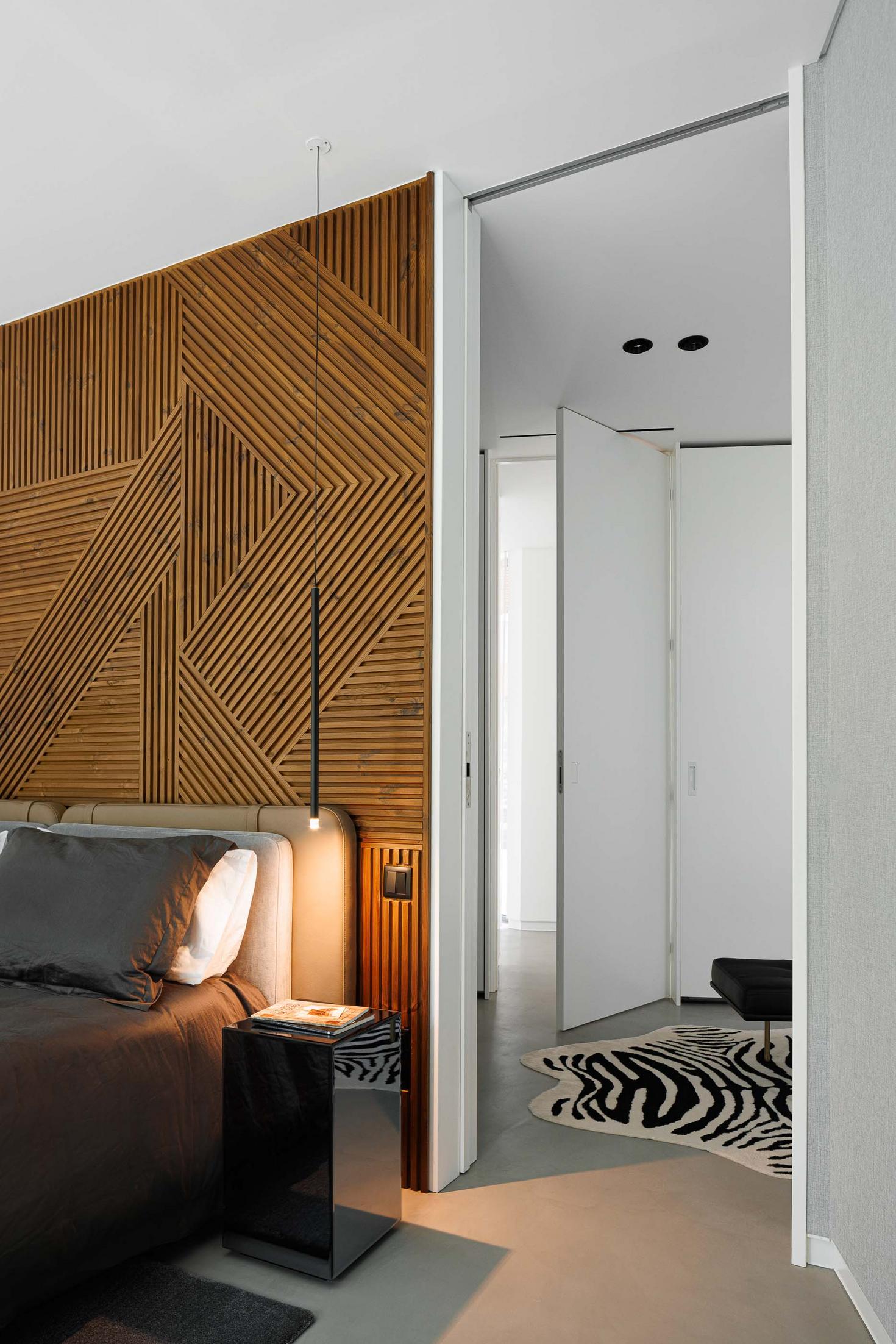 Quarto: Parede em madeira com padrão geométrico, cama com roupa cinzenta, mesa de cabeceira espelhada e alcatifa zebra. — CC House – Quinta dos Carvalhos arquitetura Inception Architects Studio em Leiria