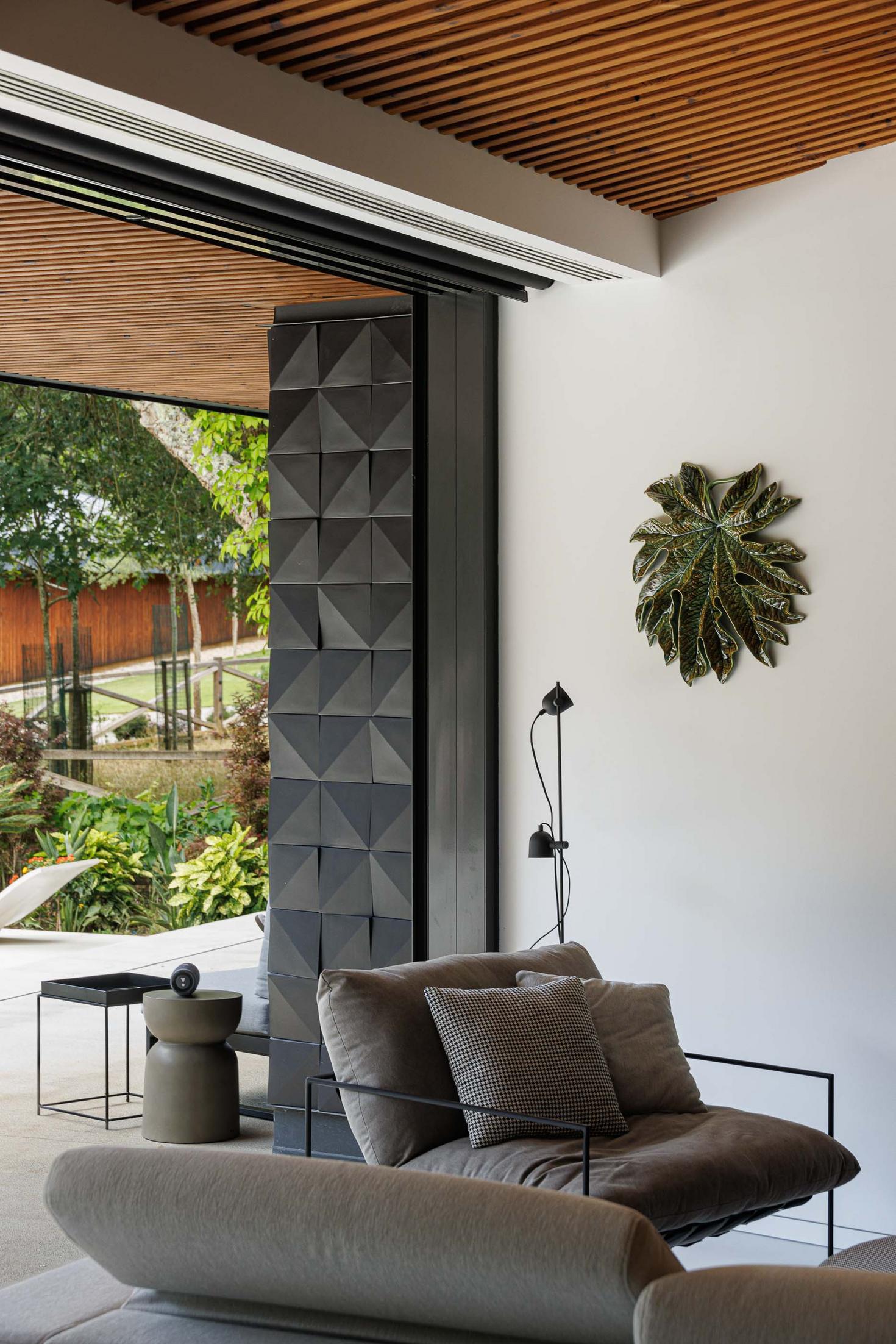 Sala de estar: Sofá cinzento, parede com revestimento em relevo geométrico e vista para o jardim. — CC House – Quinta dos Carvalhos arquitetura Inception Architects Studio em Leiria