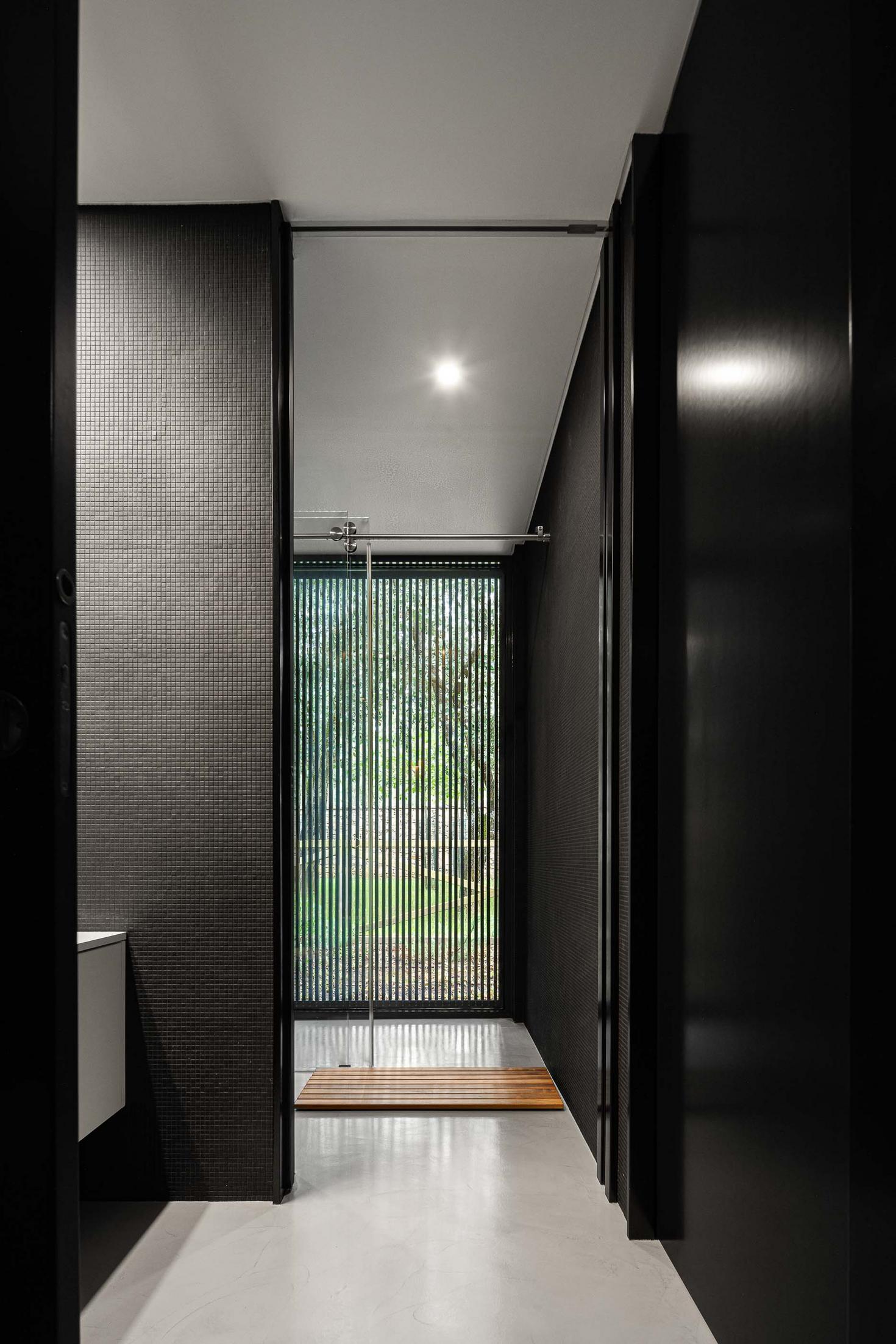 Casa de banho: Cabine de duche com ripas verticais, lavatório branco e revestimento preto texturado. — CC House – Quinta dos Carvalhos arquitetura Inception Architects Studio em Leiria