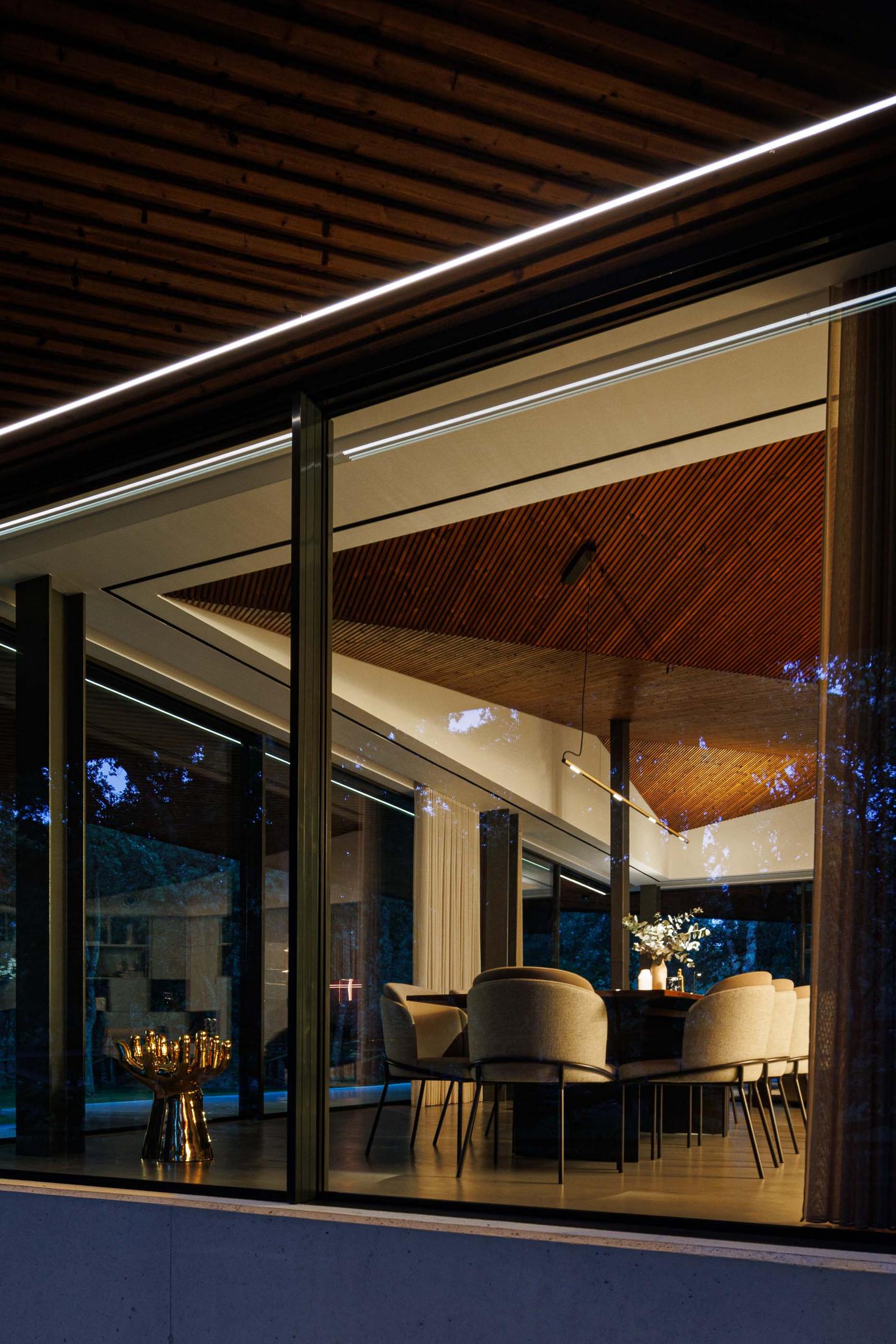 Sala de jantar: Vista da sala de jantar através da janela, teto em madeira e candeeiro suspenso linear. — CC House – Quinta dos Carvalhos arquitetura Inception Architects Studio em Leiria