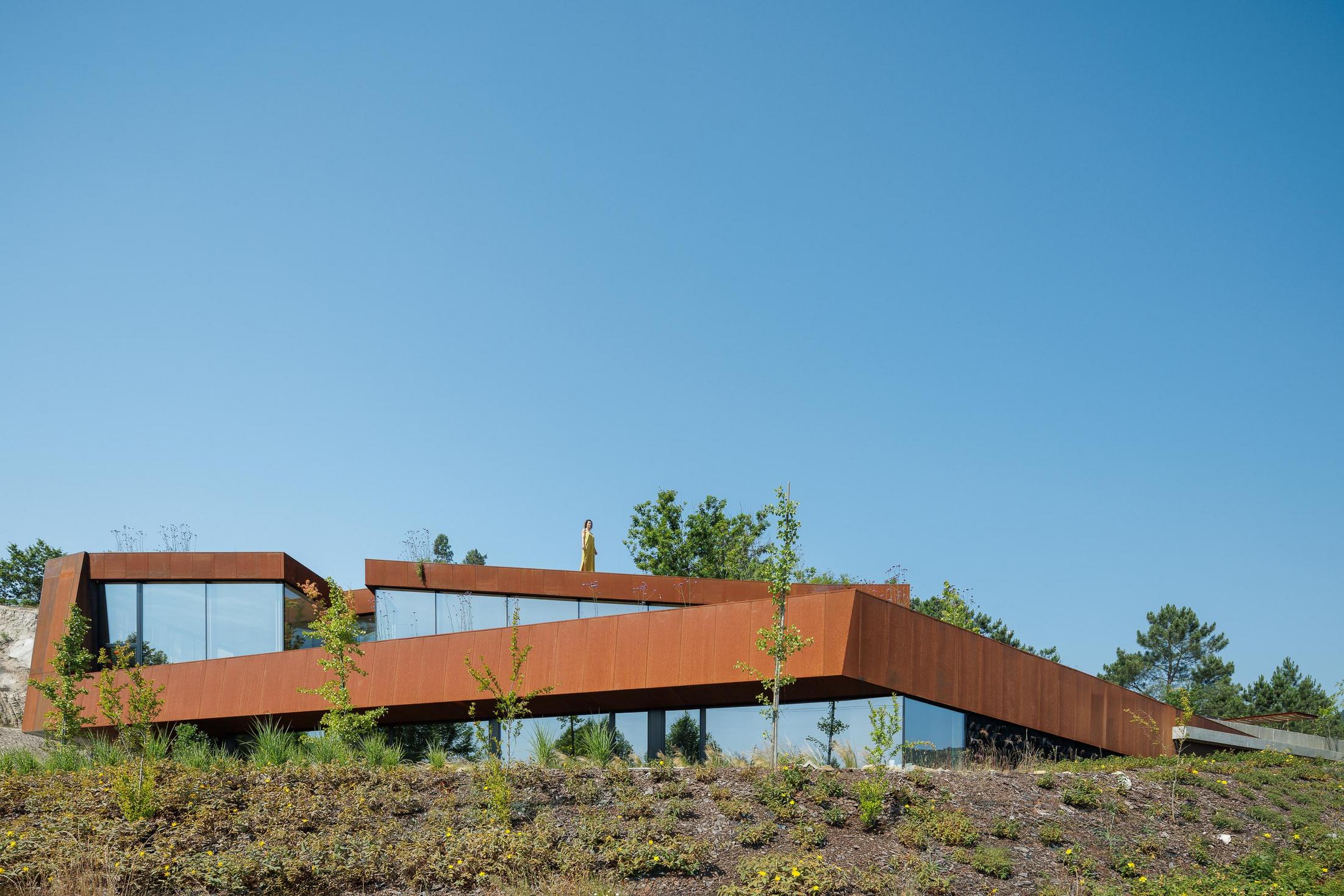 Exterior: Vista geral da casa Corten, com revestimento em aço corten e amplas janelas, integrada na paisagem natural. — Casa Corten arquitetura HPA Arquitetura e Investimentos em Celorico de Basto