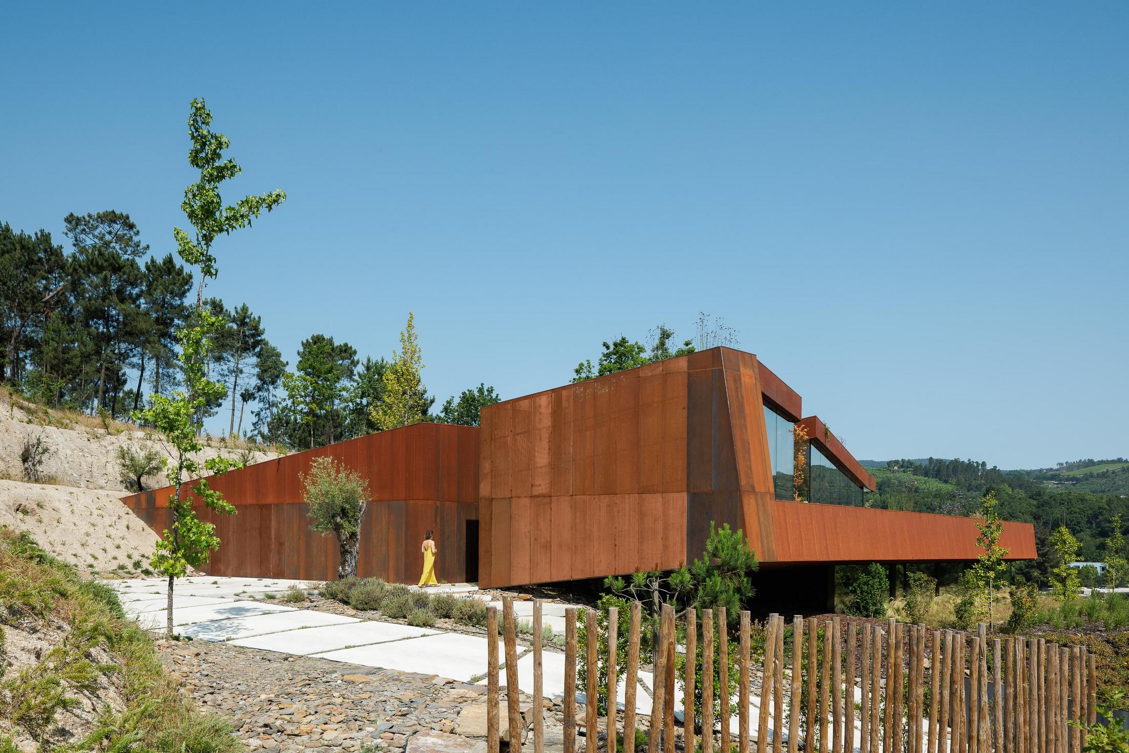 Exterior: Vista lateral da casa Corten, com caminho de acesso em lajes de pedra e vegetação envolvente. — Casa Corten arquitetura HPA Arquitetura e Investimentos em Celorico de Basto