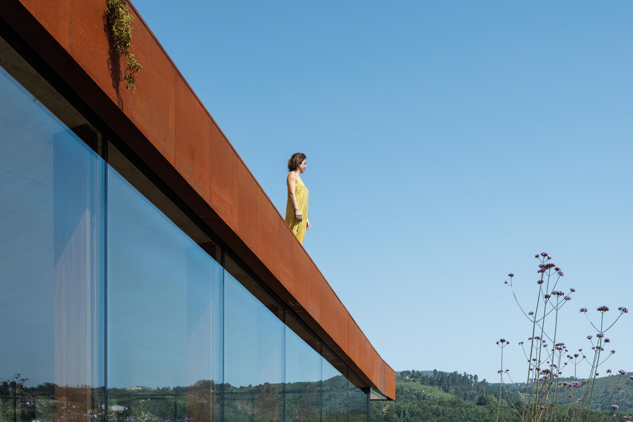 Exterior: Detalhe da fachada envidraçada com revestimento em aço corten, com uma mulher no topo da estrutura. — Casa Corten arquitetura HPA Arquitetura e Investimentos em Celorico de Basto