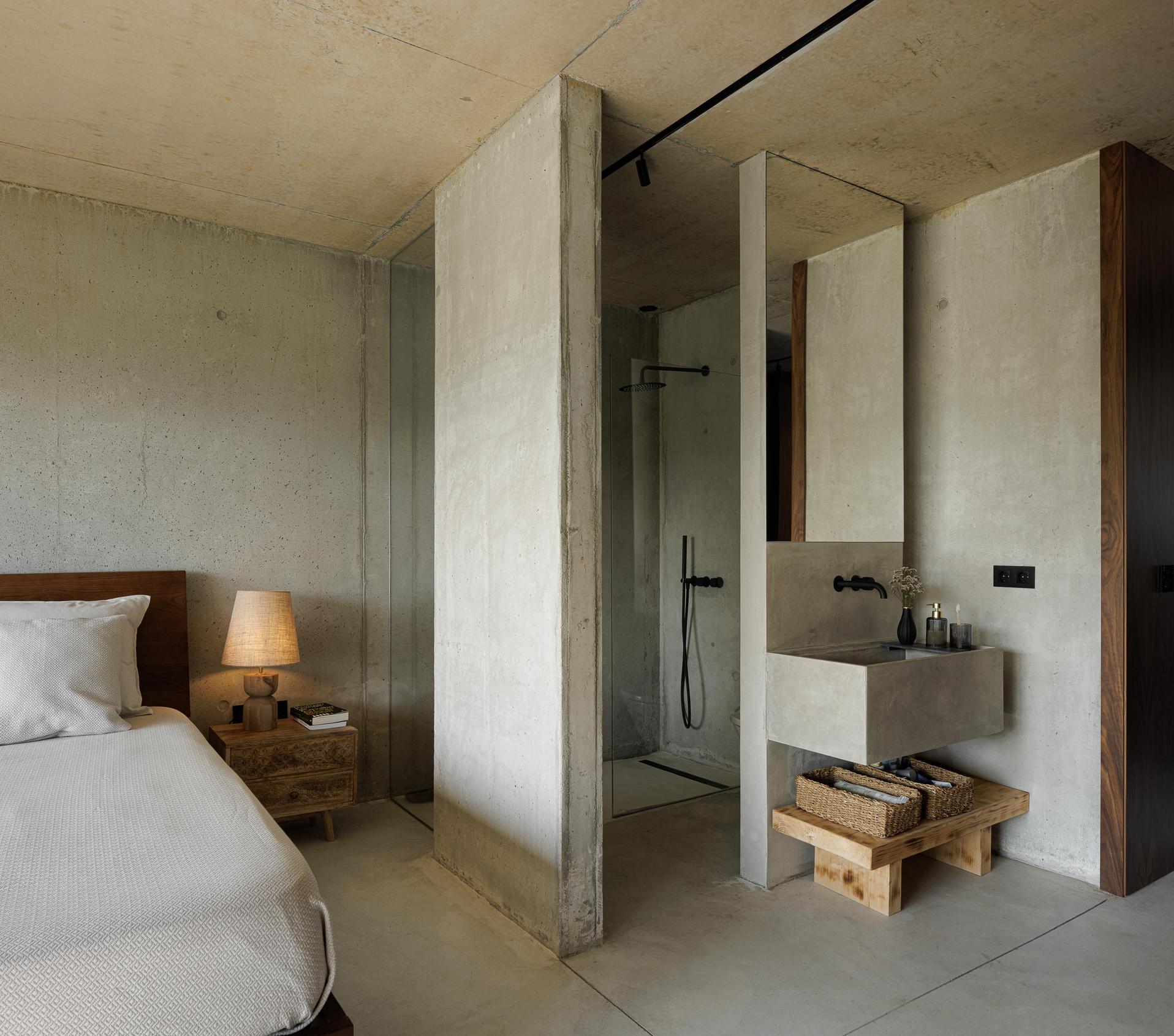 Quarto: Interior com cama de casal, casa de banho integrada com lavatório em betão e duche com divisória em vidro. — Casa Corten arquitetura HPA Arquitetura e Investimentos em Celorico de Basto