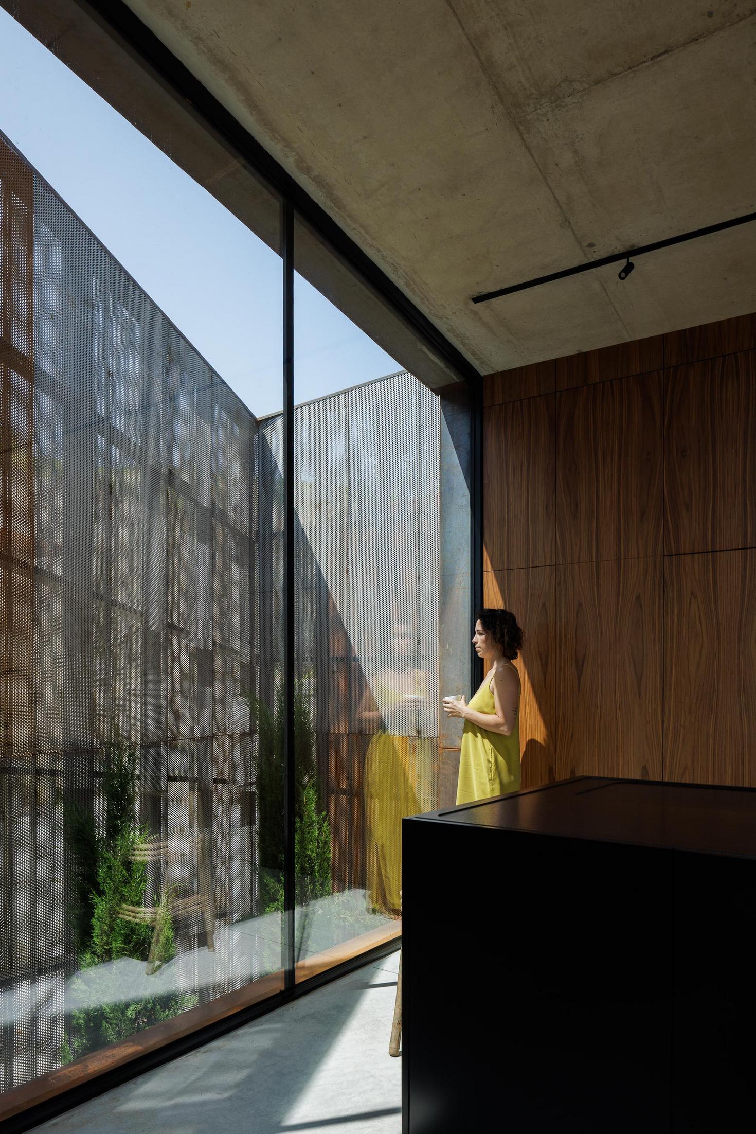 Cozinha: Detalhe de janela com tela metálica perfurada, paredes em madeira e ilha central preta. — Casa Corten arquitetura HPA Arquitetura e Investimentos em Celorico de Basto