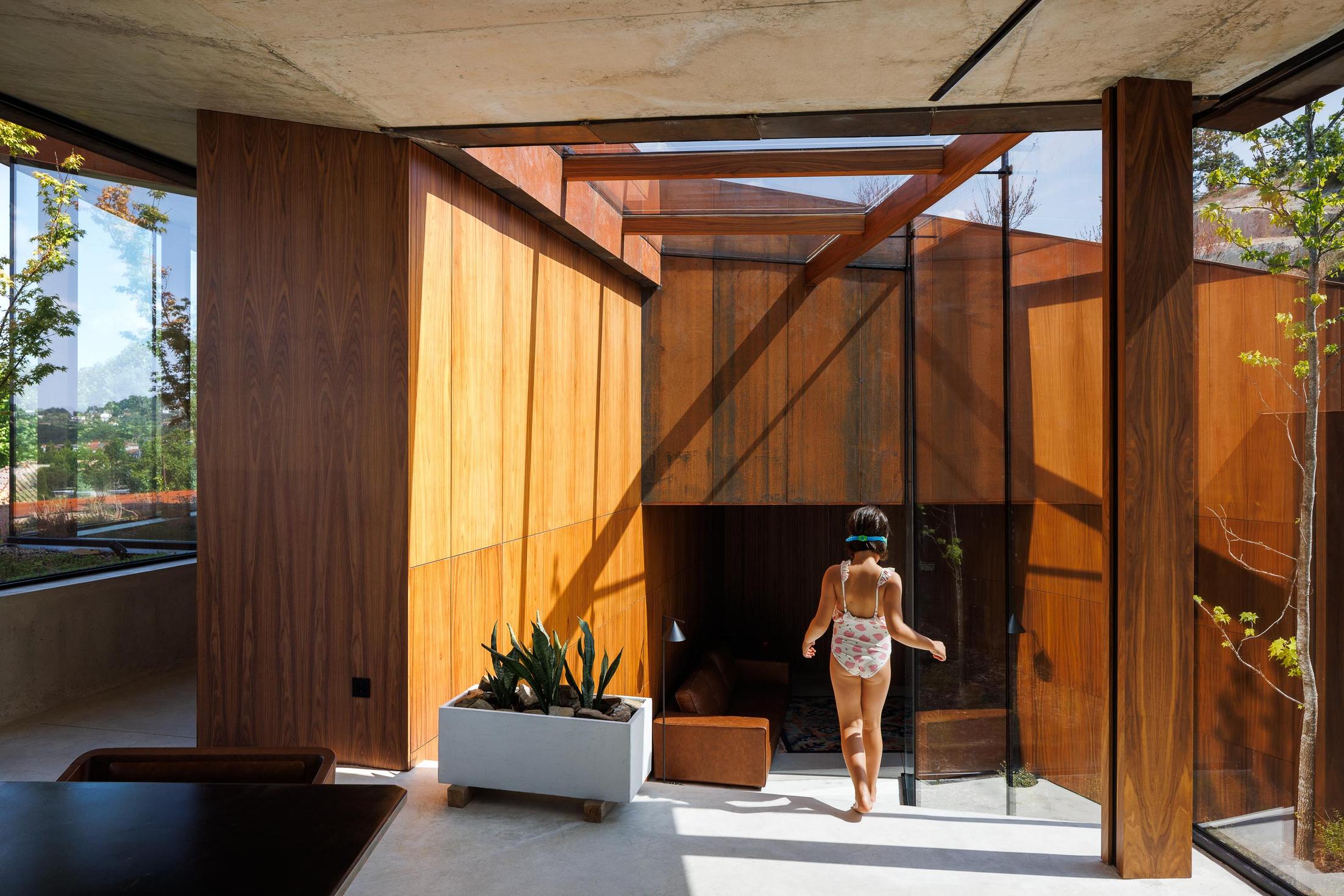 Hall: Espaço de transição com paredes em madeira, claraboia e acesso a sala de estar e escadas exteriores. — Casa Corten arquitetura HPA Arquitetura e Investimentos em Celorico de Basto
