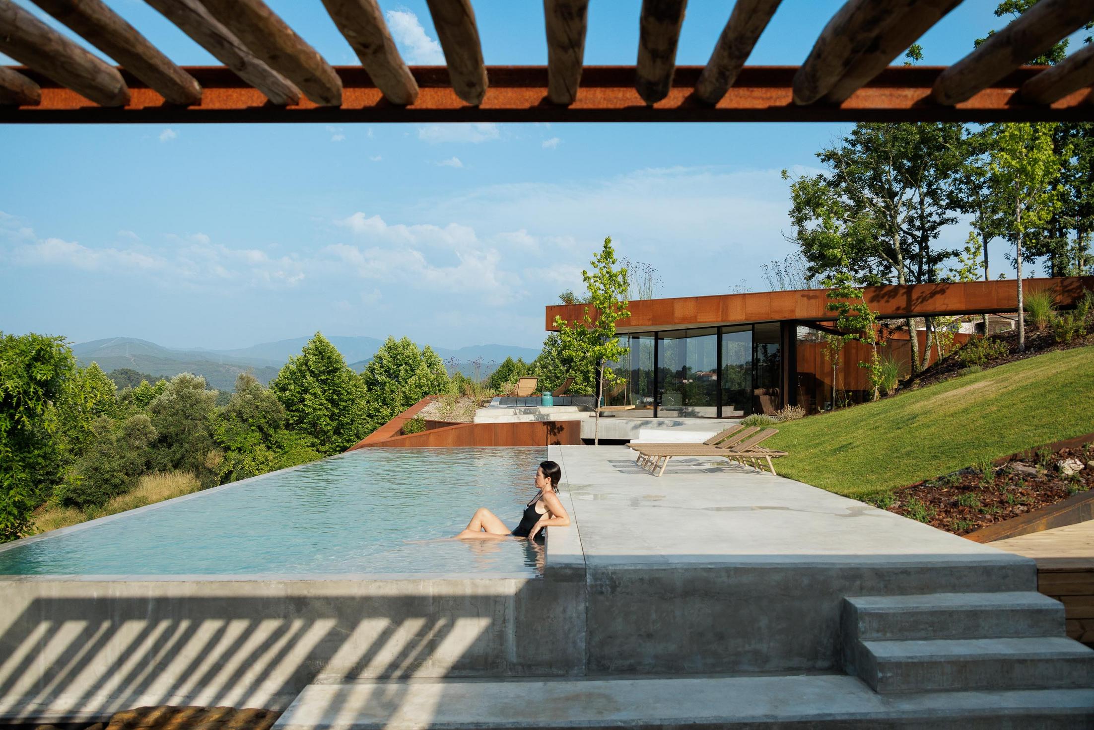 Piscina: Piscina exterior com borda infinita, espreguiçadeiras e vista panorâmica sobre a paisagem. — Casa Corten arquitetura HPA Arquitetura e Investimentos em Celorico de Basto