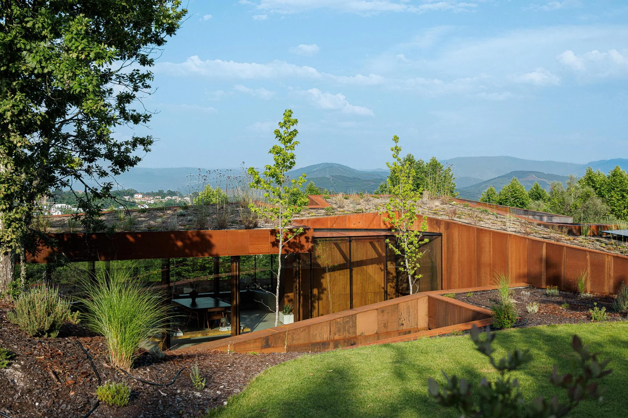 Exterior: Vista da casa com telhado verde, fachada em aço corten e zona de refeições exterior. — Casa Corten arquitetura HPA Arquitetura e Investimentos em Celorico de Basto